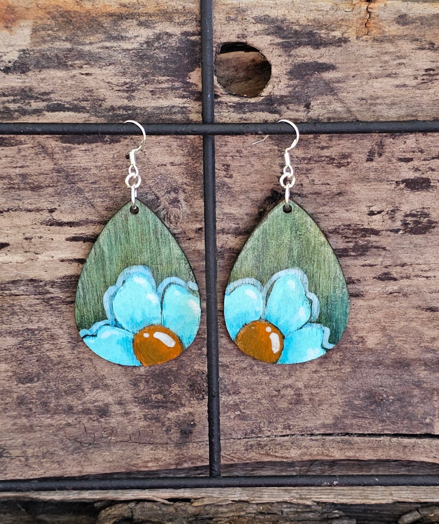 Hand Painted Ultra Lightweight Wooden Earrings. Watercolor and Acrylic. Muted green background with Turquoise Blue Daisy Flower. Teardrop in shape. Back is painted in complimentary color. Sterling Silver Findings. Hangs 2 1/4" in Length