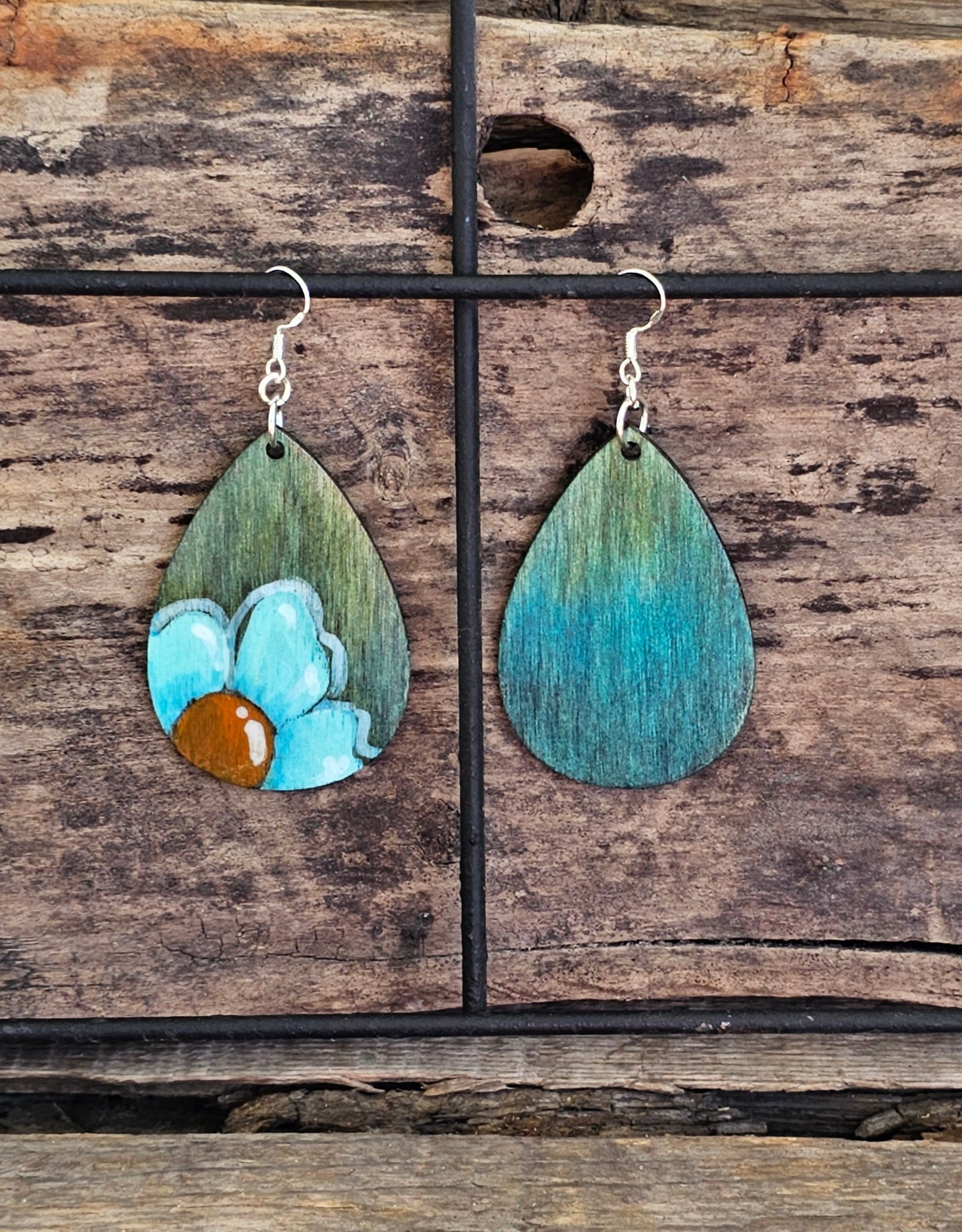 Hand Painted Ultra Lightweight Wooden Earrings. Watercolor and Acrylic. Muted green background with Turquoise Blue Daisy Flower. Teardrop in shape. Back is painted in complimentary color. Sterling Silver Findings. Hangs 2 1/4" in Length