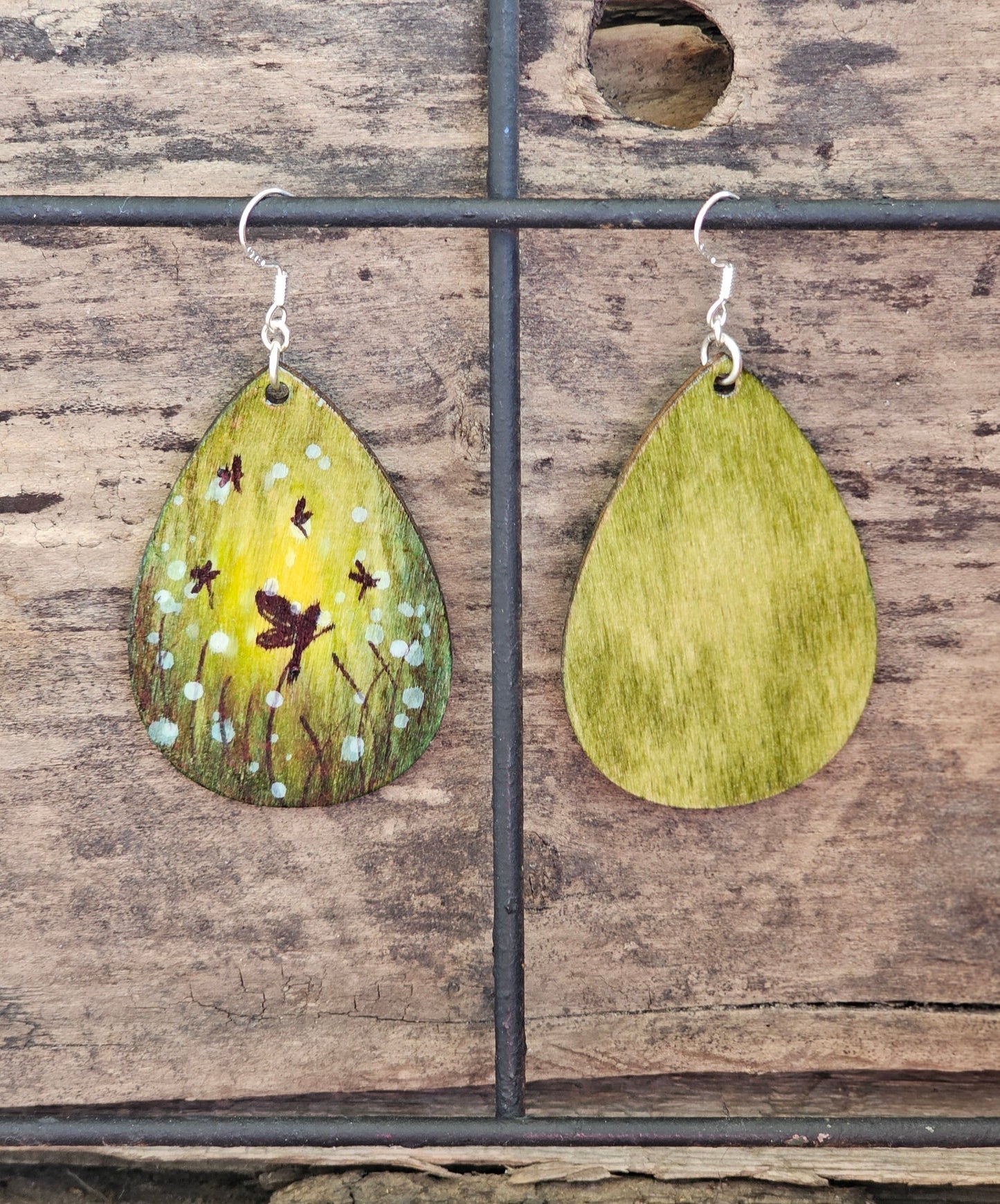 Hand Painted Ultra Lightweight Wooden Earrings. Watercolor and Acrylic. Multi toned Green colored background. Dragonfly Fairies, Mystical Forest . Teardrop in shape. Back is painted in complimentary color. Sterling Silver Findings. Hangs 2 1/4" in Length