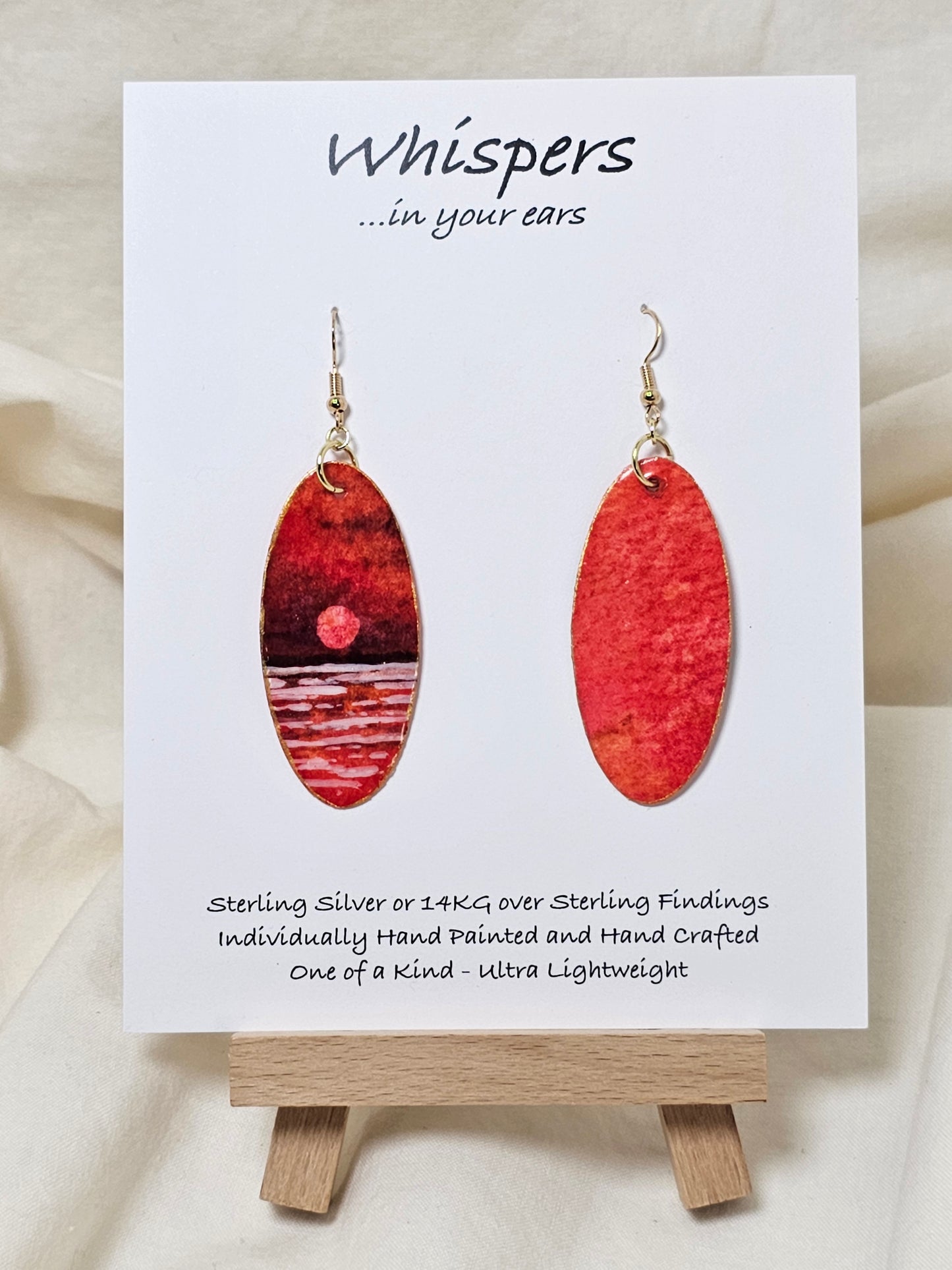 Red Sky Morning Hand Painted Paper Earrings. Ultra lightweight elongated 2" oval. Watercolor red, orange, white and gold sunrise over water. Back painted in similar color. Resin coating for durability. 14KG over sterling findings. Hangs 2 1/4" in length