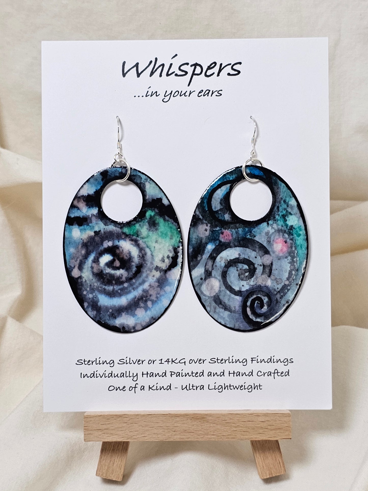 Cosmic Energy Hand Painted Paper Earrings. Ultra lightweight 2 1/2" Statement Oval with small circular cut out. Watercolor blues, greens and black. Abstract design. Back is painted in similar colors. Resin coating for durability. Sterling Silver findings. Hangs 2 3/4" in length