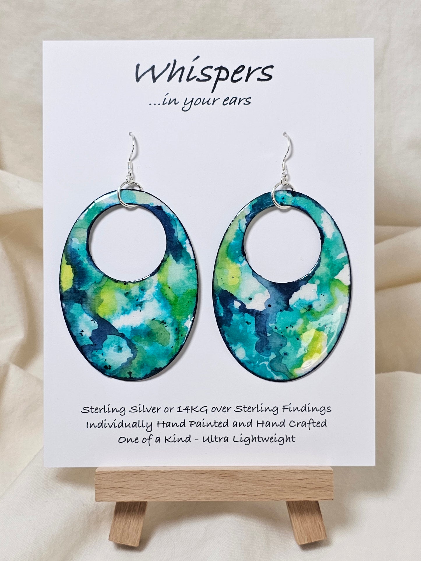 Caribbean Waters Hand Painted Paper Earrings. Ultra lightweight 2 1/2" Statement Oval with medium circular cut out. Watercolor blues, greens and turquoise. Abstract design. Back is painted in similar colors. Resin coating for durability. Sterling Silver findings. Hangs 2 3/4" in length