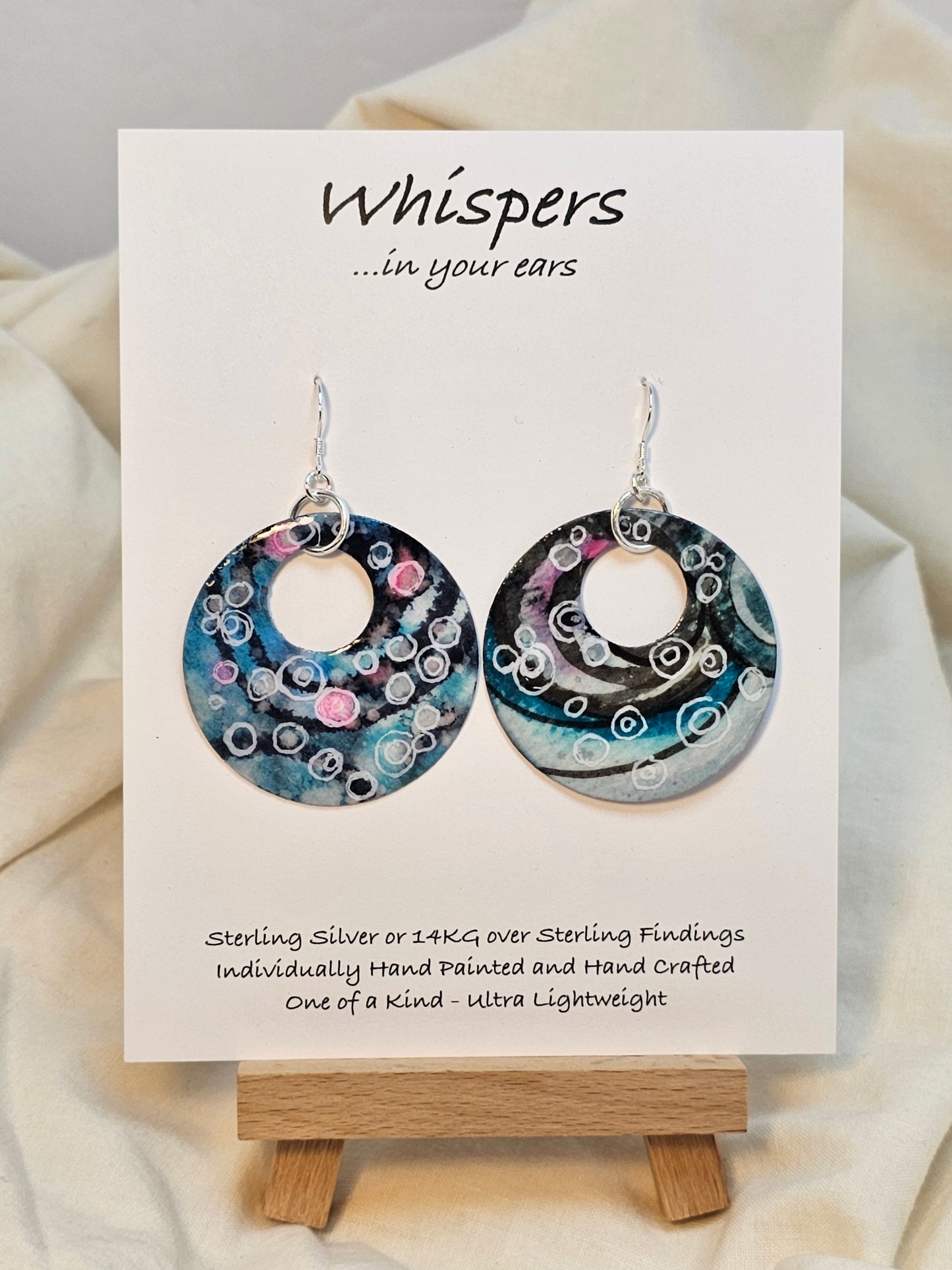Bubbles Hand painted watercolor paper earrings. Ultra lightweight. Dark blue, pink, light pink, turquoise with white circles . Back is painted with similar color and design. Large circular in shape with circular cut out. Resin coating for durability. Sterling silver findings. Hangs 2" in Length