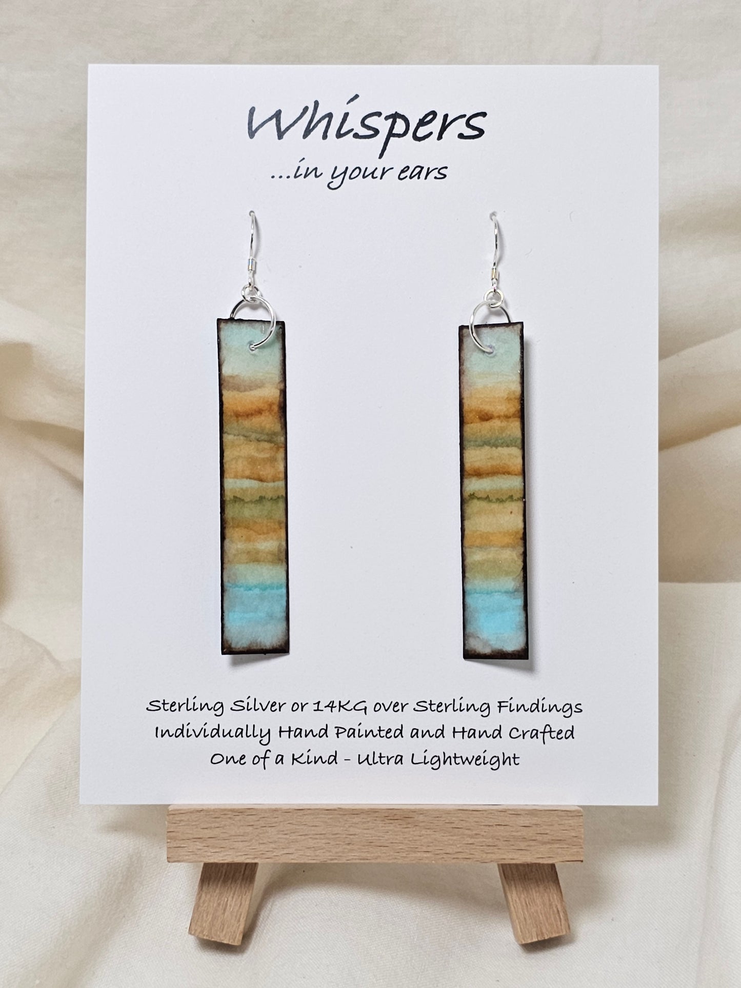 Vintage Beach Reflections Hand Painted Paper Earrings. Ultra lightweight 1/2" x 2 1/2" elongated rectangle. Watercolor abstract beach reflection. Distressed edge in brown. Back is painted with similar design. Resin coating for durability. Sterling Silver findings. Hangs 2 3/4" in length