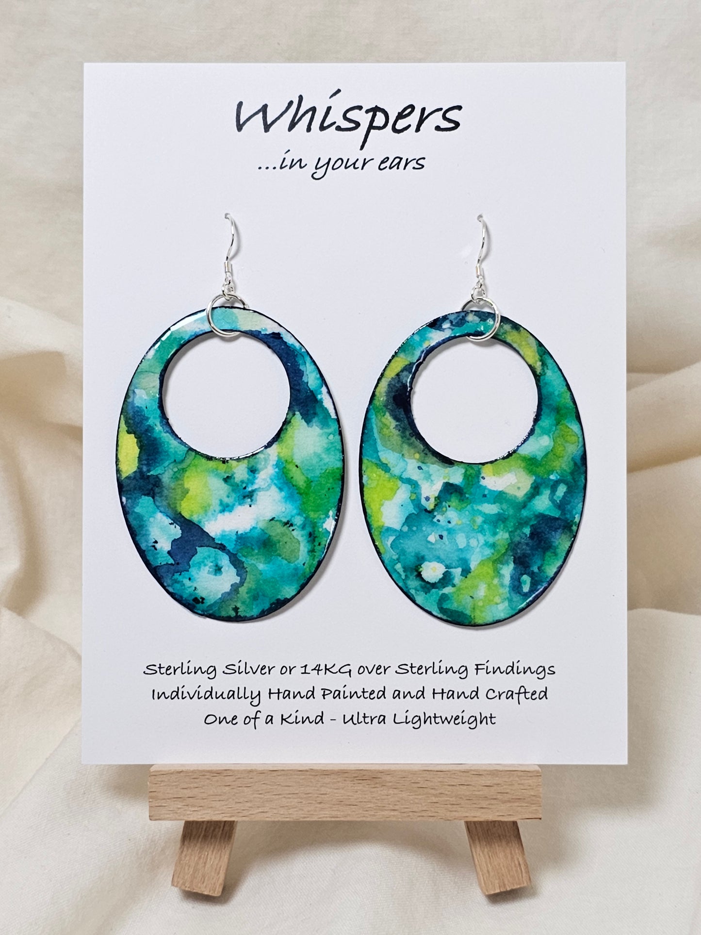 Caribbean Waters Hand Painted Paper Earrings. Ultra lightweight 2 1/2" Statement Oval with medium circular cut out. Watercolor blues, greens and turquoise. Abstract design. Back is painted in similar colors. Resin coating for durability. Sterling Silver findings. Hangs 2 3/4" in length