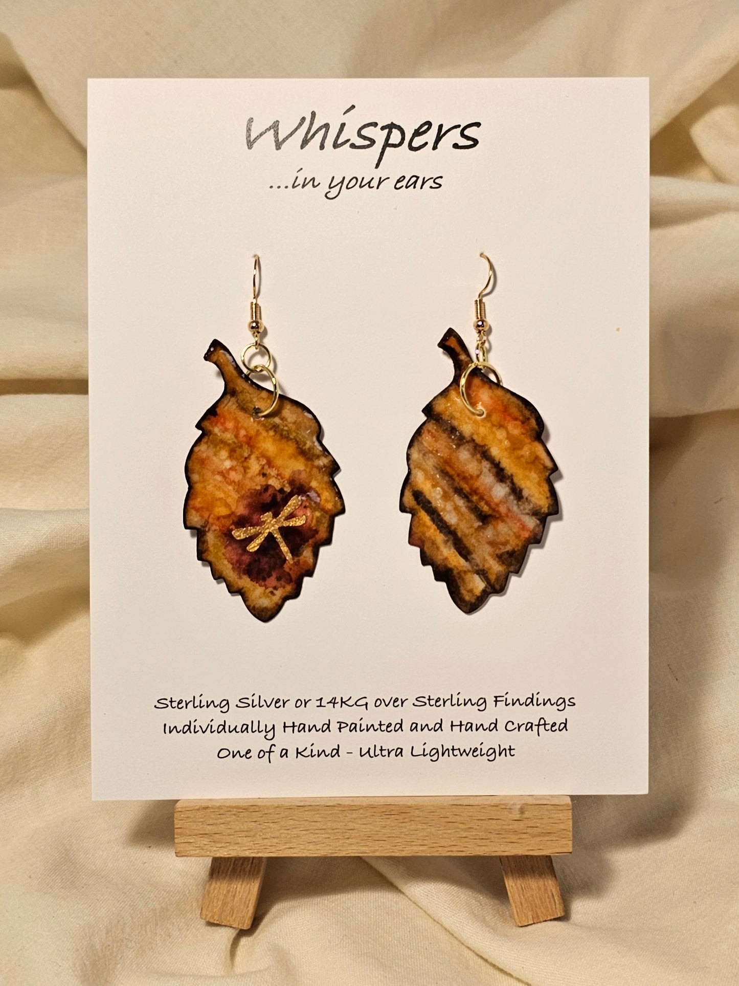 Golden Dragonfly Leaf Hand Painted Paper Earrings. Ultra light weight. 2" Leaf shape. Painted in rust and muted red tones with Golden paper dragonfly atop. Outlined in Dark brown. Back is painted in similar design. 14kg over Sterling Silver ear wires and findings. Resin coating for durability. Hangs 2"