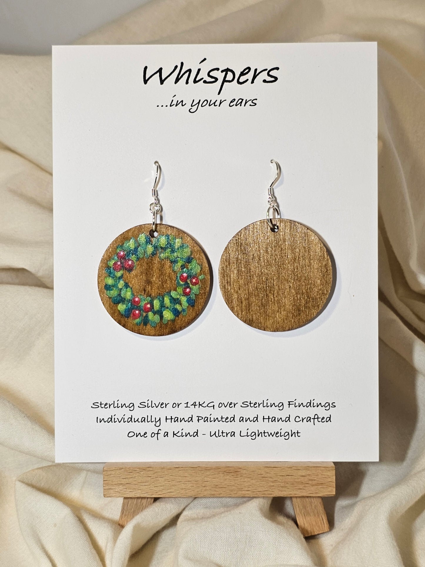 Holly Wreath Hand Painted Wood Earrings. 1 1/2" Stained wood round, two toned Holiday wreath painted with red berries. Back of earring is stained. Enameled for durability. Sterling Silver findings. Hangs 1 3/4"