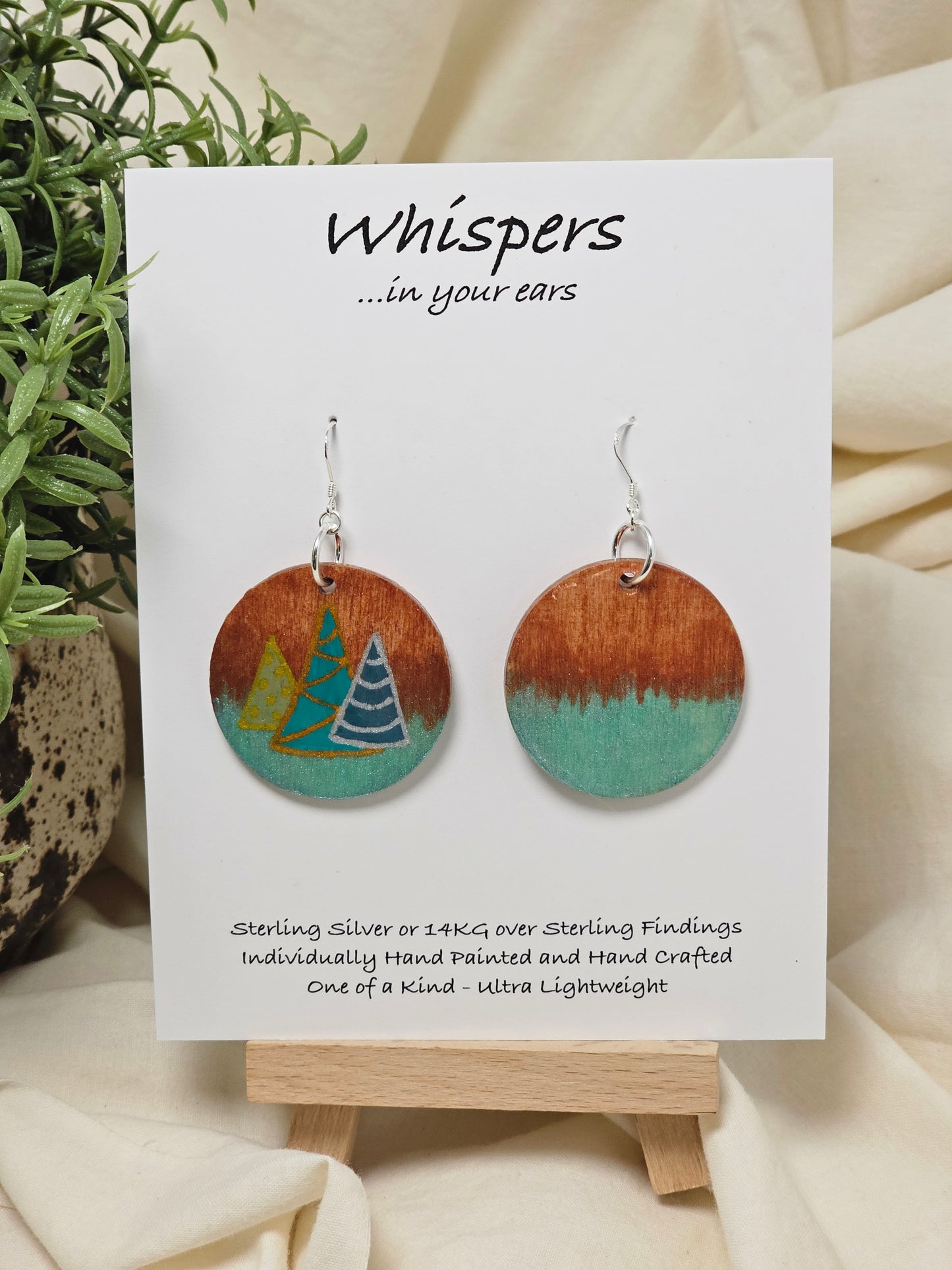 Three Modern Trees Hand Painted Wood Earrings. 1 1/2" wood round, two toned 3 Holiday trees painted with metallic colors .Back of earring is painted with copper and light iridescent green. Resin coated for durability. Sterling Silver findings. Hangs 1 3/4"