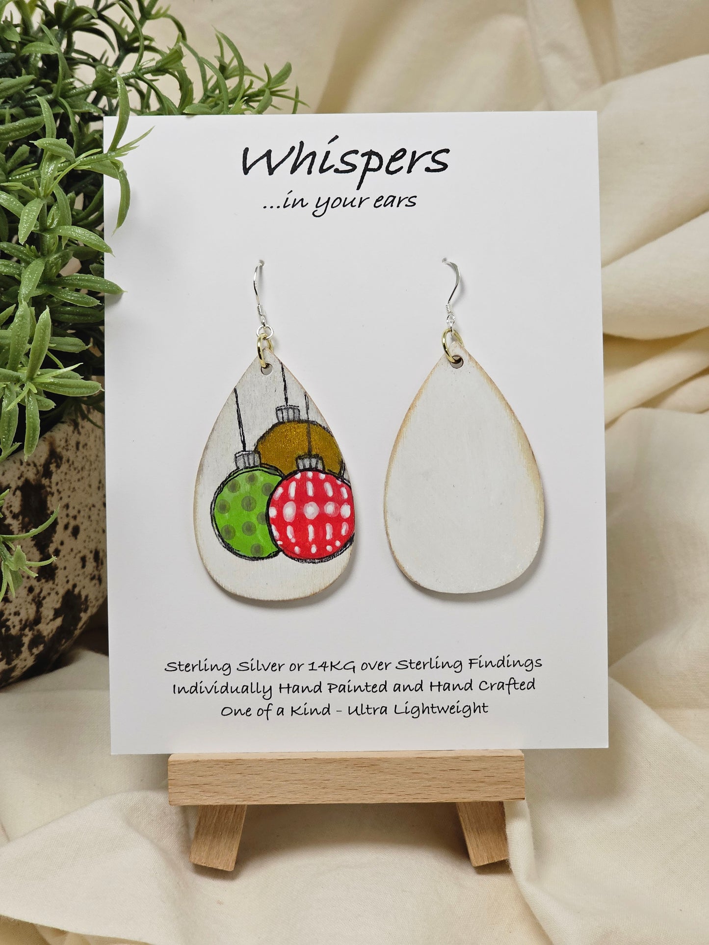 Ornament Trio Hand Painted Wood Earrings. 2" Wood Tear Drop painted white background. Three hand painted. Pattern Ornaments painted red, green and copper, outlined in black. Back is painted white. Distressed edge. Enameled for durability. Sterling Silver ear wires and findings. Ultra light weight. Hangs 2 1/2"