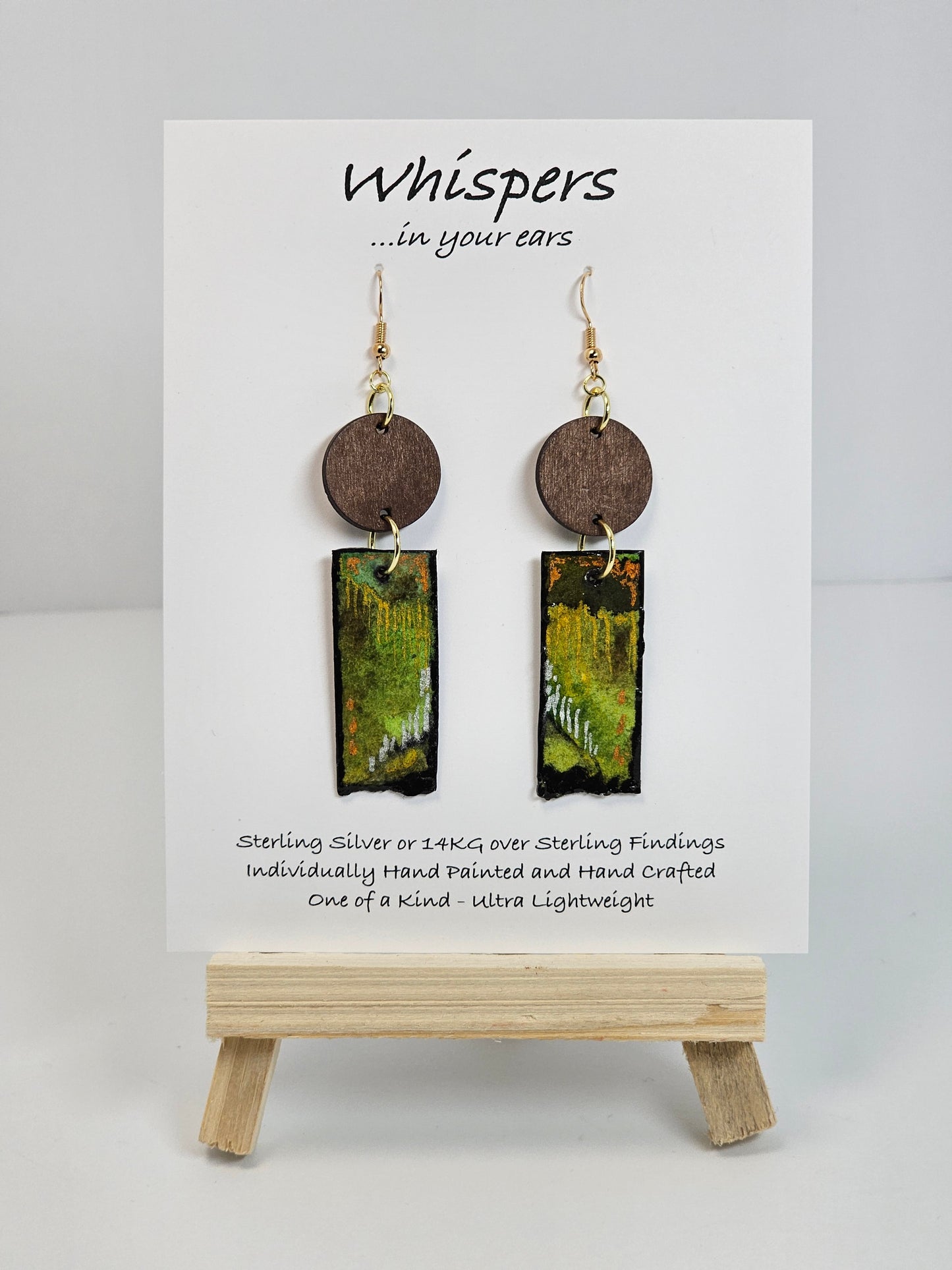 Copper, Green and Black Abstract Motif Hand Painted Paper and Wood Earrings. 1/2" x 1 5/8" Paper Rectangle hand painted brightly colored background with silver and copper accents. Edged in black. Hanging from embellished wooden disc dark brown. Back is painted to match. Resin coating for durability. Sterling Silver findings. Hangs 2 1/2" in length
