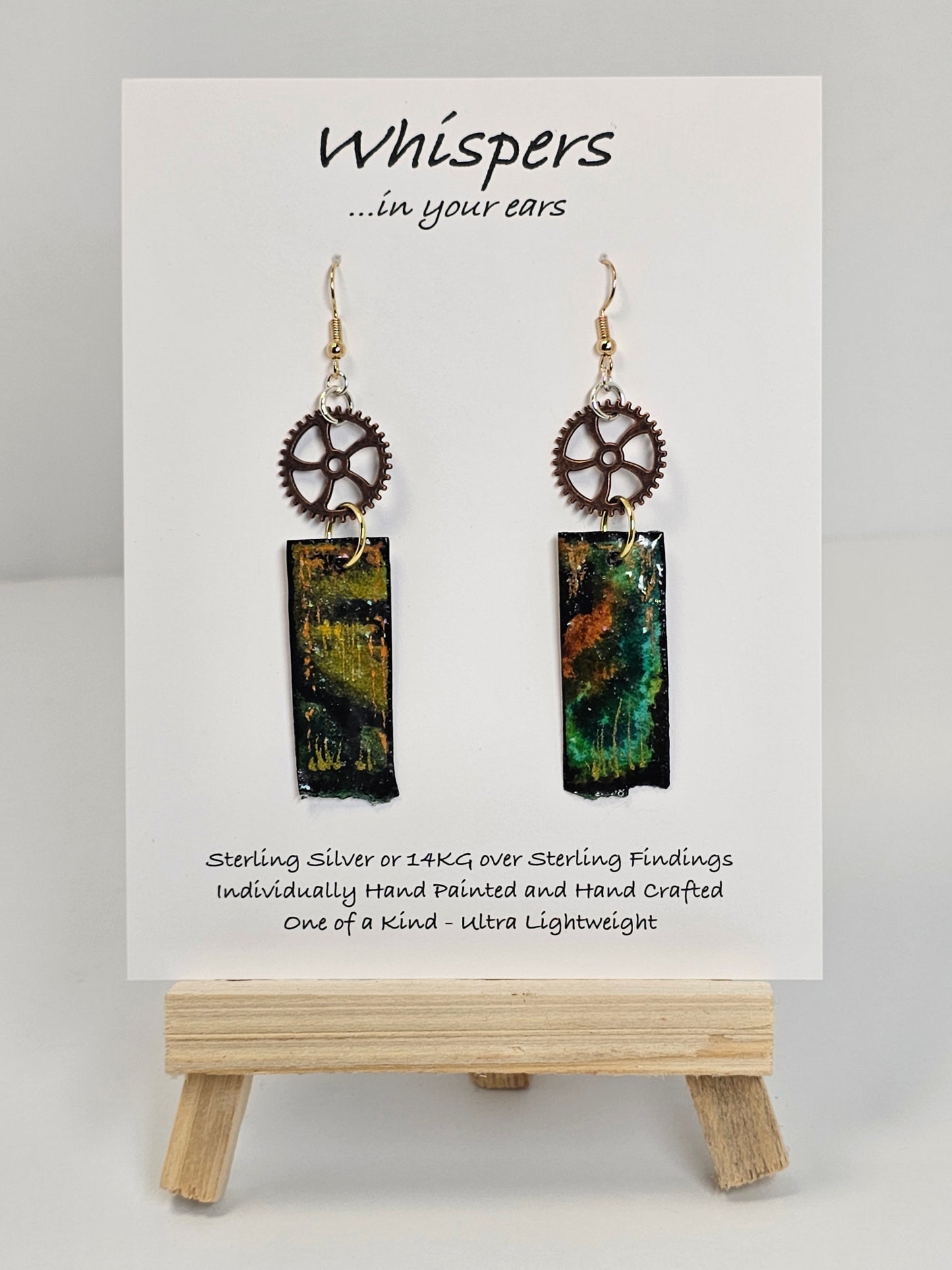 Copper Steampunk Hand Painted Paper and Wood Earrings. 1/2" x 1 5/8" Paper Rectangle hand painted brightly colored background with silver and copper accents. Edged in black. Hanging from Copper notched circular gear. Back is painted to match. Resin coating for durability. Sterling Silver findings. Hangs 2 1/2" in length