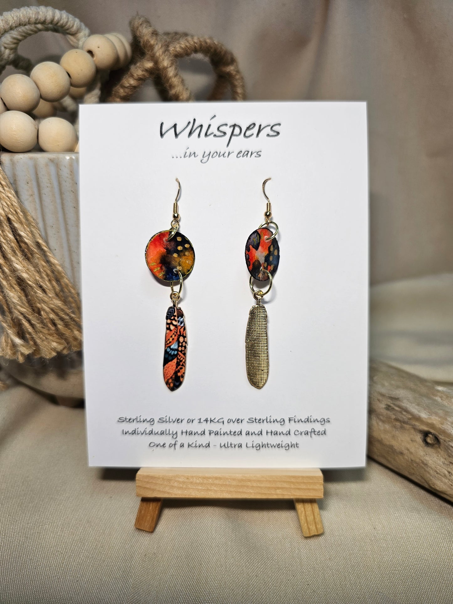 Gold Dot Feathers Hand Painted Paper Earrings. 3/4" circular hand painted paper earring. Below hangs a gorgeous light weight metal enameled feather charm pendant. Back is gold in color. Reds, blues, metallic accents edged in gold. Back of paper is painted in similar design and colors. Resin coated for durability. 14kg over sterling silver ear wires and findings. Hangs 2 1/2" in length