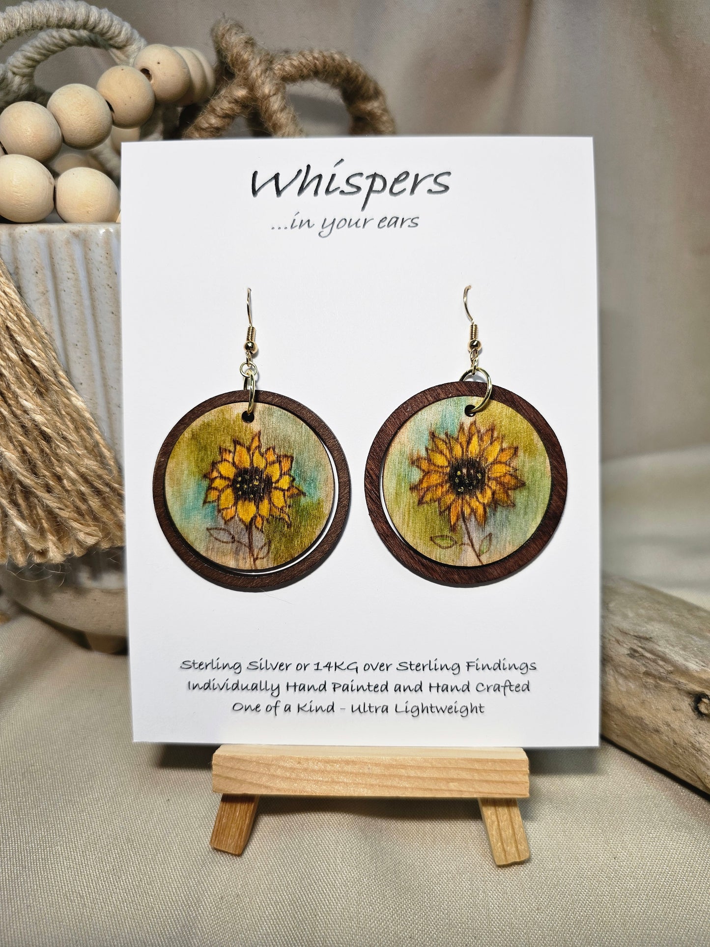 Sunflower Wash Hand Painted Wood Earrings. 1 1/2" wooden round. Hangs inside larger dark stained wood circle pendant. Sunflower painted in watercolor. Yellow, aqua blues, green and brown. Ultra light weight. Back of earring is painted with similar design. Enameled for durability. 14kg over Sterling silver ear wires and findings. Hangs 2"