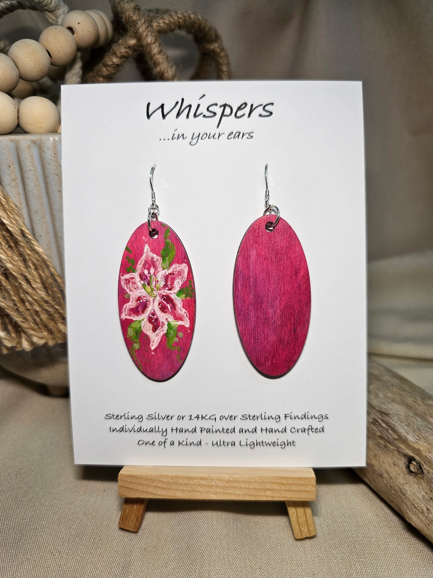 Pink Lily Bloom Hand Painted Wood Earrings. Lily floral bloom, painted in acrylics. Back is painted in similar color. Ultra light weight. Enameled for durability. 2" Elongated wood oval. Sterling silver mixed metals with sterling silver findings and hangs 2 1/4" in length