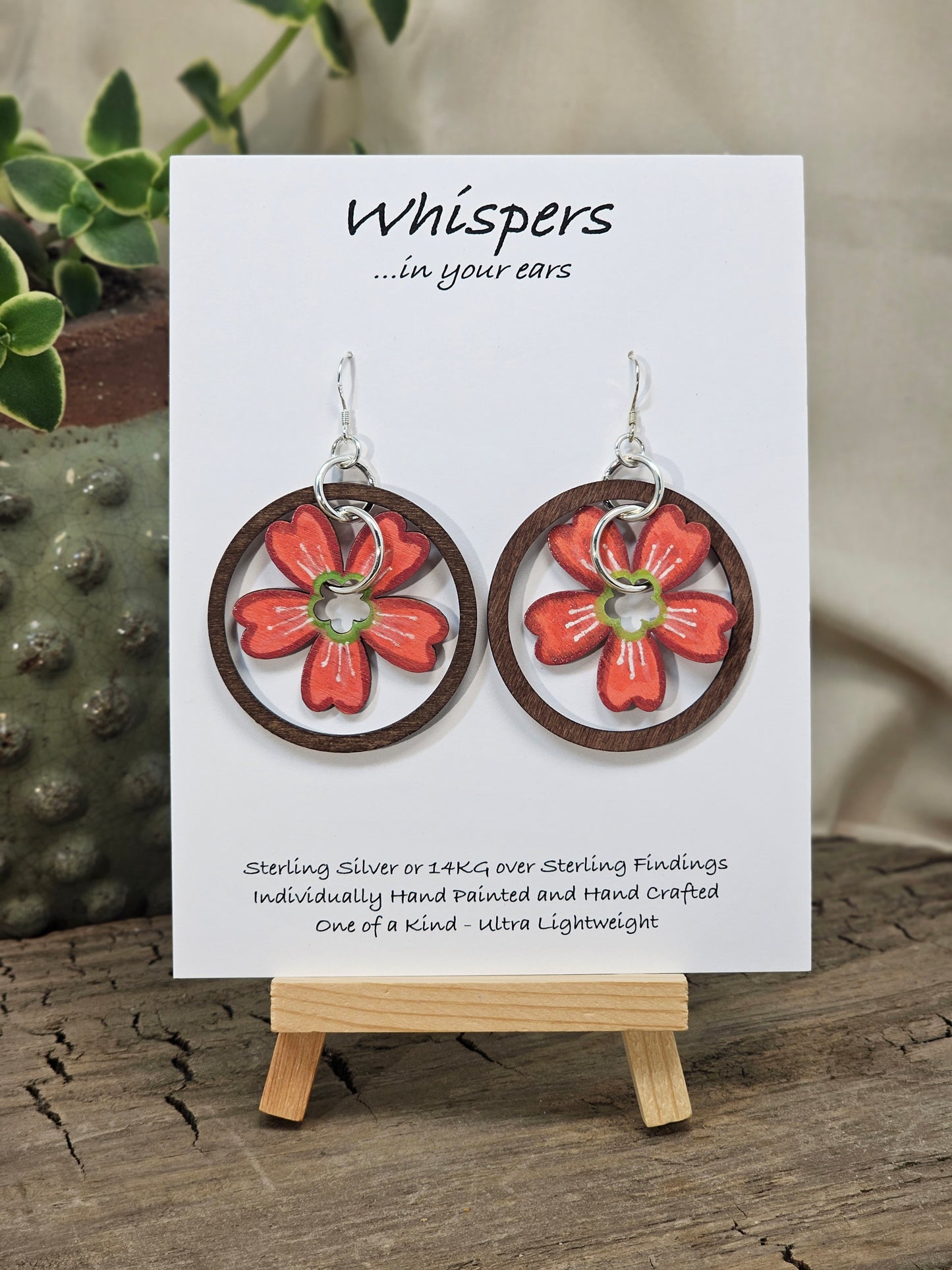 Hawaiian Plumeria Hand Painted/Crafted Earrings. These gorgeous one of a kind Statement earrings are hand painted wooden flower die cut in coral. green and white and have the same design on both sides. Sterling Silver Ear wires and large findings. Large dark stained wood circle encompasses the piece. Enameled for durability. Hangs 2" Ultra light weight