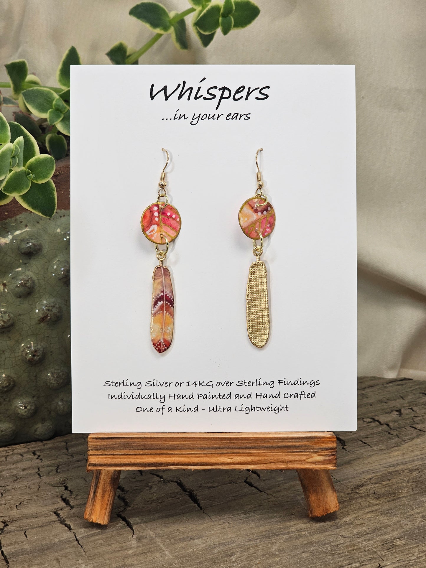 White Dot Feathers Hand Painted Paper Earrings. 5/8" circular hand painted paper earring. Below hangs a gorgeous light weight metal enameled feather charm pendant. Back is gold in color. Coral, peach and white, metallic accents edged in gold. Back of paper is painted in similar design and colors. Resin coated for durability. 14kg over sterling silver ear wires and findings. Hangs 2 1/2" in length