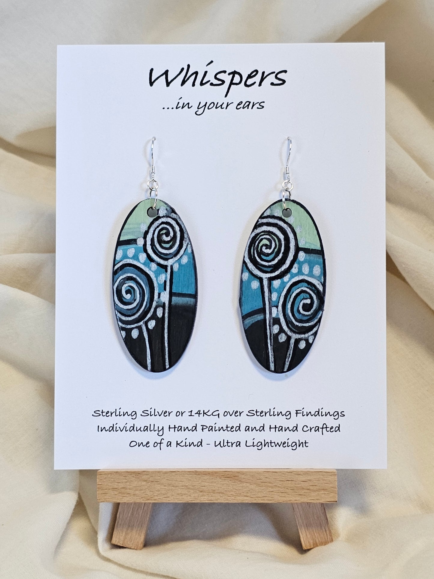 Silver Dandelion Puffball Hand Painted Wood Earrings. Geometric background in soft green, aqua blue and black. Back painted in similar design. Resin coated for durability. 2" Elongated oval wood. Sterling silver findings and hangs 2 1/4"