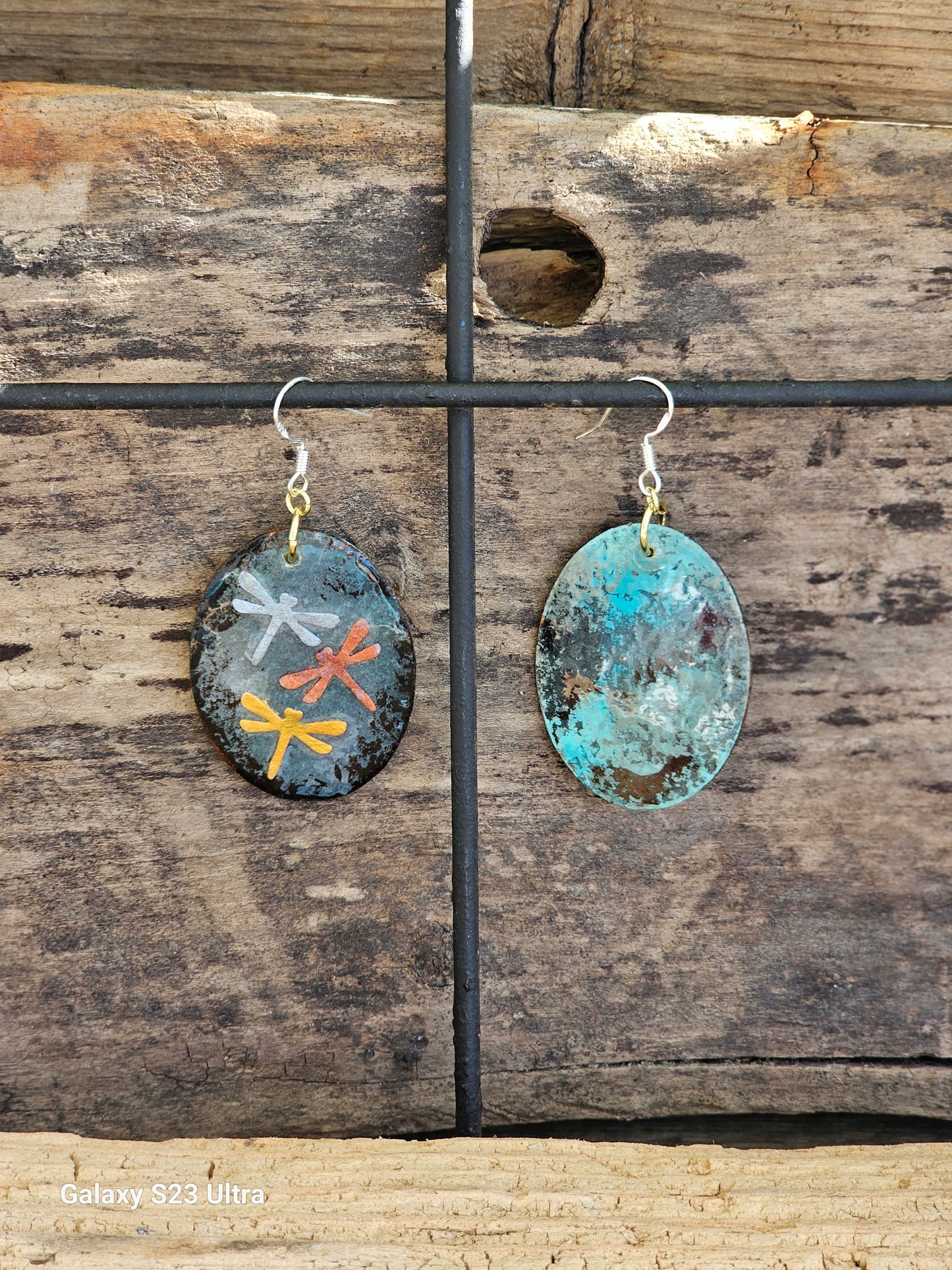 Hand painted Watercolor Mixed Media Collage Dragonfly Trinity. Ultra lightweight paper earrings. Grey blue patina background.  Layered collage with copper, silver and gold painted paper dragonflies.  Edged in dark brown patina. Back is painted in complimentary color. Oval in shape. Combination of14kg over sterling silver  and Sterling silver findings. Hangs 1 3/4" in Length