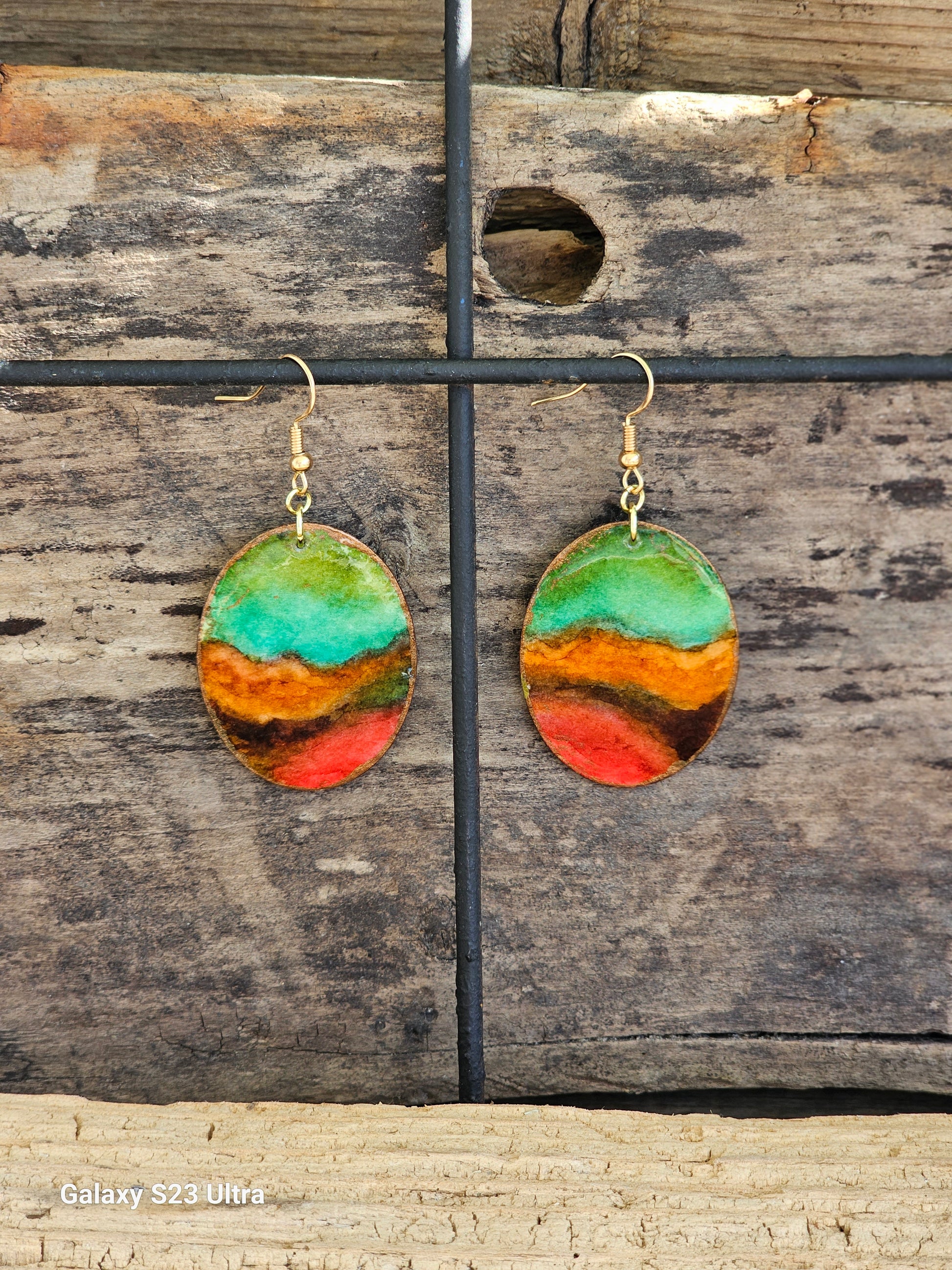 Hand painted Watercolor Desert View Nature scape. Ultra lightweight paper earrings. Teal blue, orange, red and brown background landscape.  Edged in golds. Back is painted in complimentary color. Oval in shape. 14kg over sterling silver findings. Hangs 1 3/4" in Length