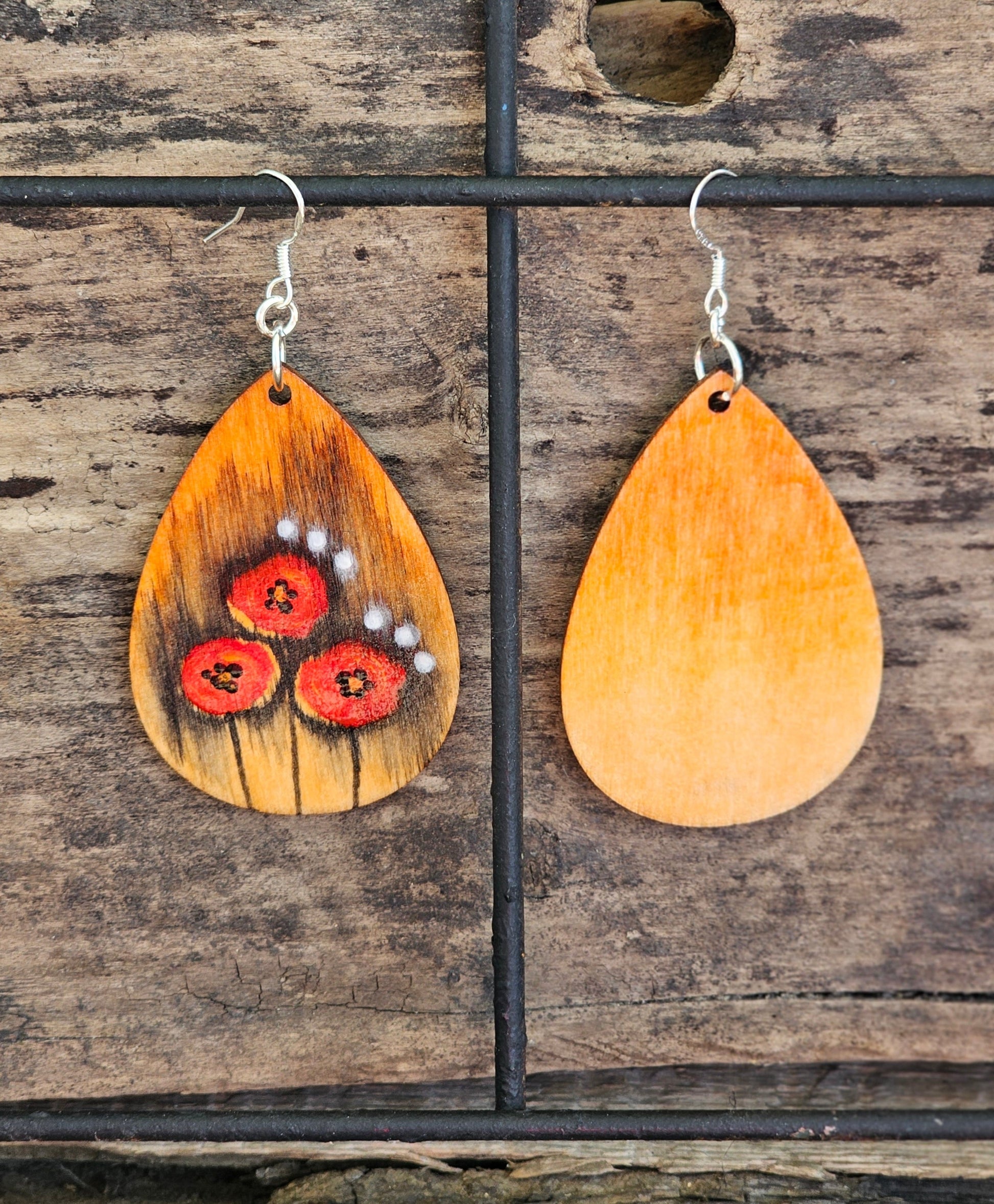 Hand Painted Ultra Lightweight Wooden Earrings. Watercolor and Acrylic.  Pale Orange colored  background. Trio of Red Poppies, black shadows and white accent dot design. Teardrop in shape. Back is painted in complimentary color. Sterling Silver Findings. Hangs 2 1/4" in Length