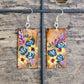 Hand painted Watercolor and Acrylic Floral Teal Rose and Rudbeckia. Ultra lightweight paper earrings. Faux wood background with yellow and teal flowers .  Edged in brown. Back is painted in complimentary color. Rectangular in shape. Sterling silver findings. Hangs 2 1/8" in Length