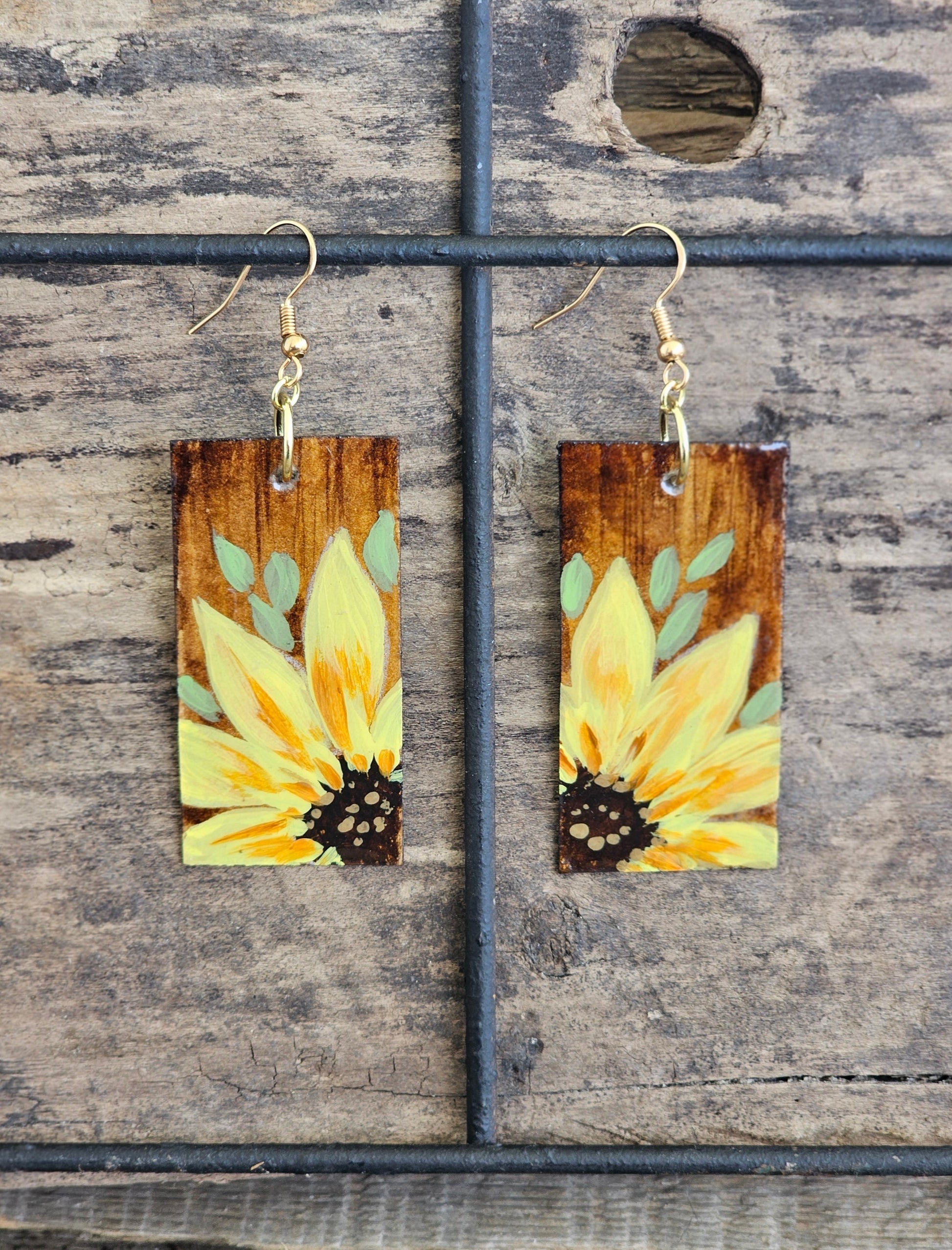 Hand painted Watercolor and Acrylic Sunflowers. Ultra lightweight paper earrings. Faux wood background with Yellow Sunflowers .  Edged in brown. Back is painted in complimentary faux wood. Rectangular in shape. 14kg over sterling silver findings. Hangs 2 1/8" in Length