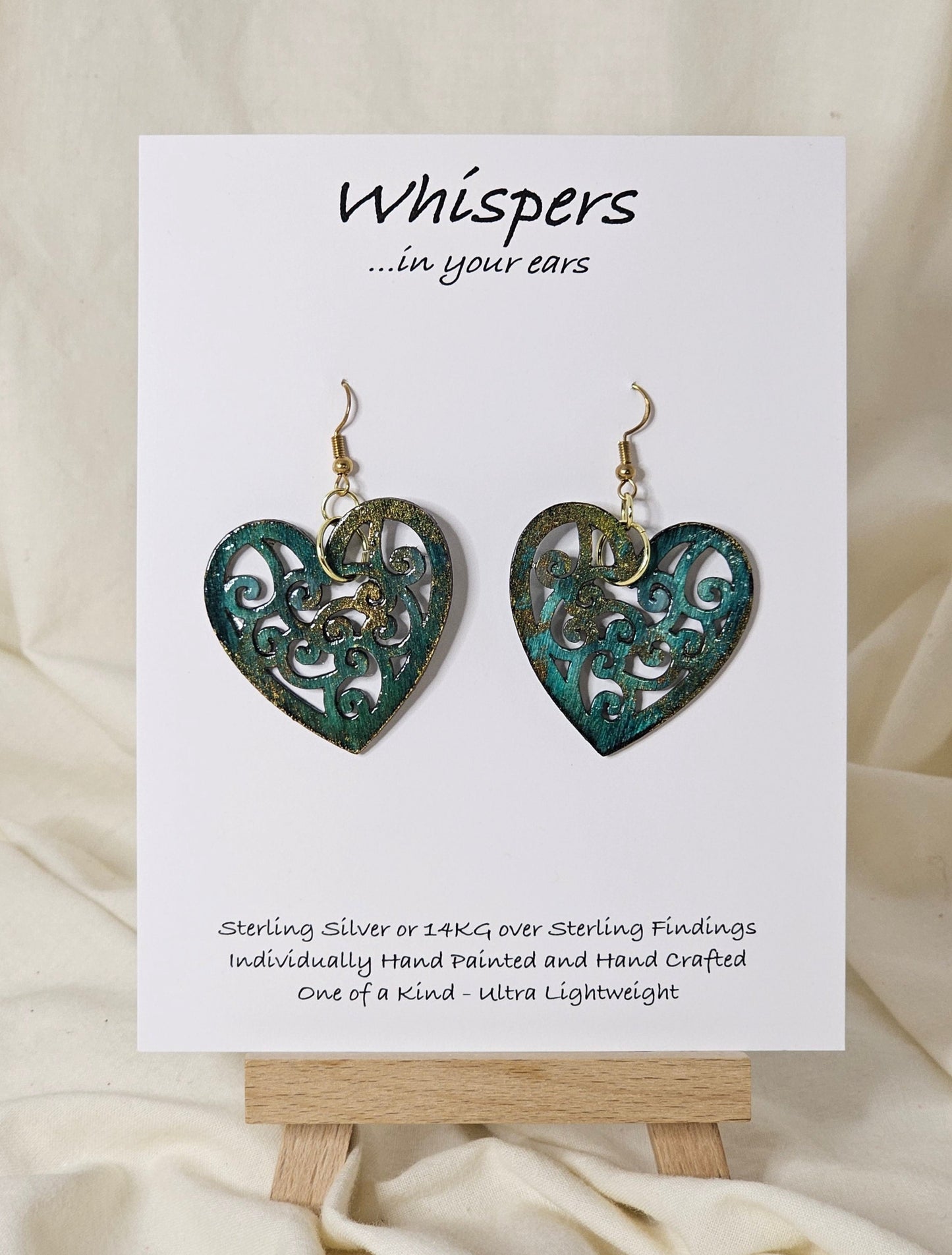 Heart Earrings Wood die cut hand painted. Faux Patinaed metal green, teal, bronze and gold. Filigree pattern. Enameled for durability. Back is painted in the same color and pattern.  Heart is 1 1/2 " in width. 14 kg over silver findings. Hangs 1 1/2" in length 