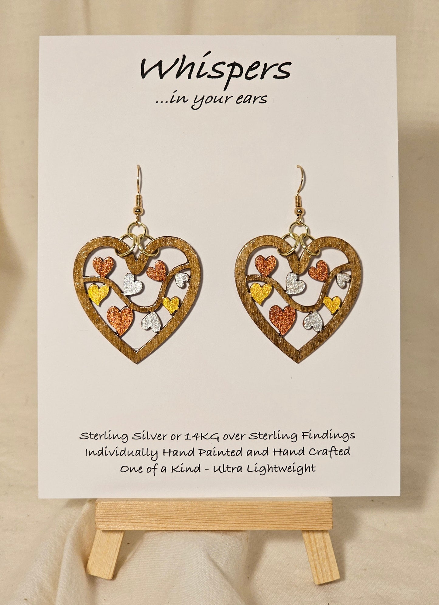 Metallic Hearts Wood Die cut hand Painted Earrings. Small hearts on a vine individually painted in gold, silver and copper. Back is painted to match. 1 1/2" Heart. Enameled for durability. 14KG over sterling findings Hangs 1 3/4" in length