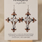 Metallic Iron Cross Hand Painted Statement Wood Cross. Painted in Silver, Bronze and Iron Black. Fleur-de-lis die cut details. 2 5/8" Cross. Back is painted to match. Enameled for durability. Sterling Silver findings. Hangs 3" in length