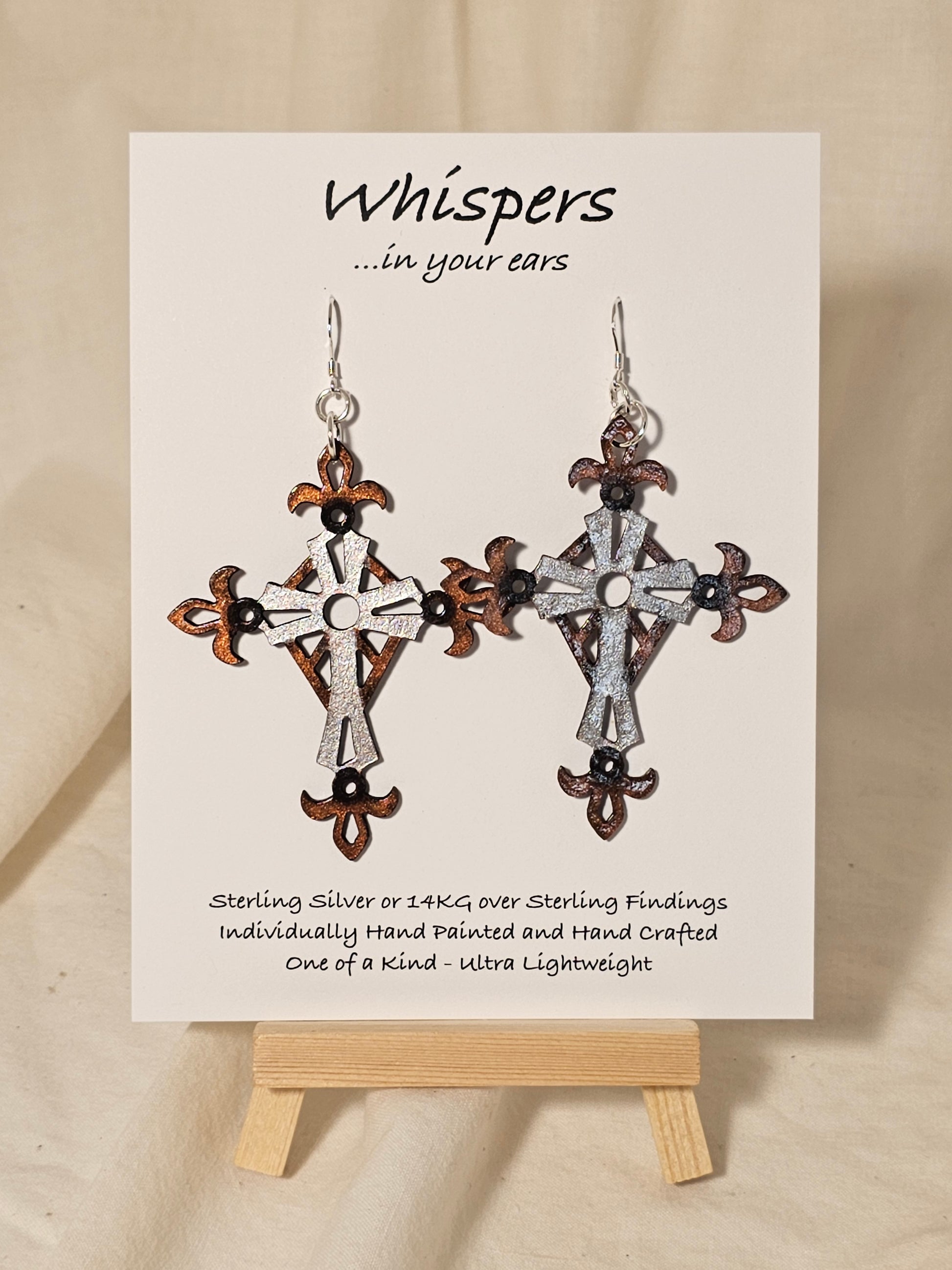 Metallic Iron Cross Hand Painted Statement Wood Cross. Painted in Silver, Bronze and Iron Black. Fleur-de-lis die cut details. 2 5/8" Cross. Back is painted to match. Enameled for durability. Sterling Silver findings. Hangs 3" in length