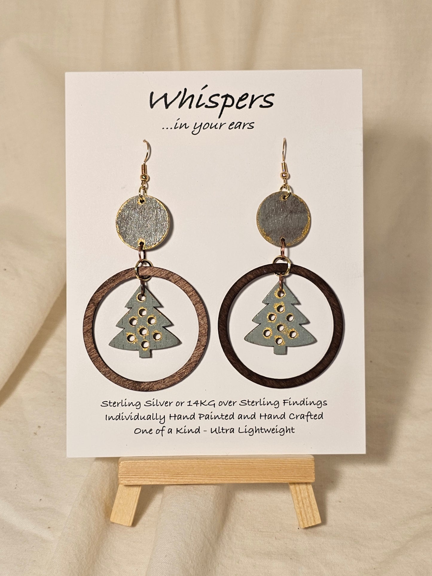 Christmas Tree Hand Painted Wood Earrings. Sage green, walnut and gold large statement piece. Wood disk, open wood circle with hanging wooden tree pendant. Back is painted to match. Enameled for durability. 14KG over sterling findings. Hangs 3" in length.