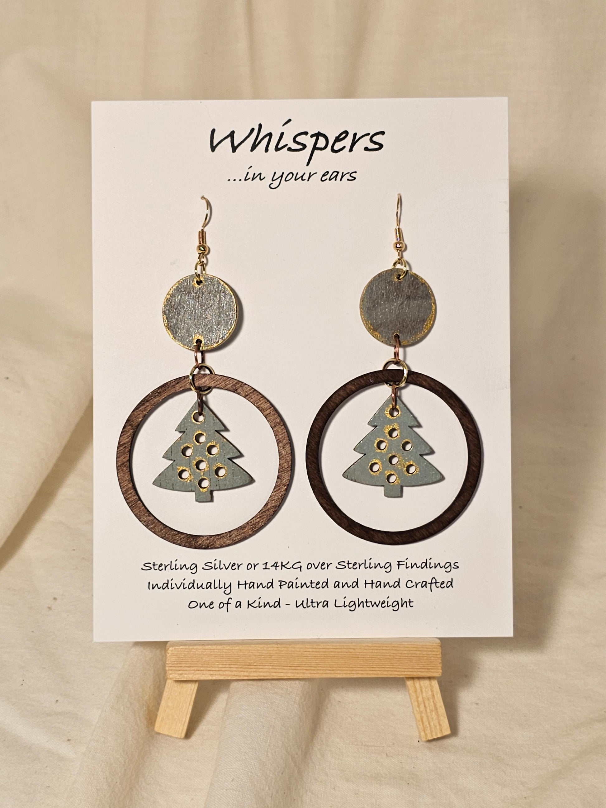 Christmas Tree Hand Painted Wood Earrings. Sage green, walnut and gold large statement piece. Wood disk, open wood circle with hanging wooden tree pendant. Back is painted to match. Enameled for durability. 14KG over sterling findings. Hangs 3" in length.