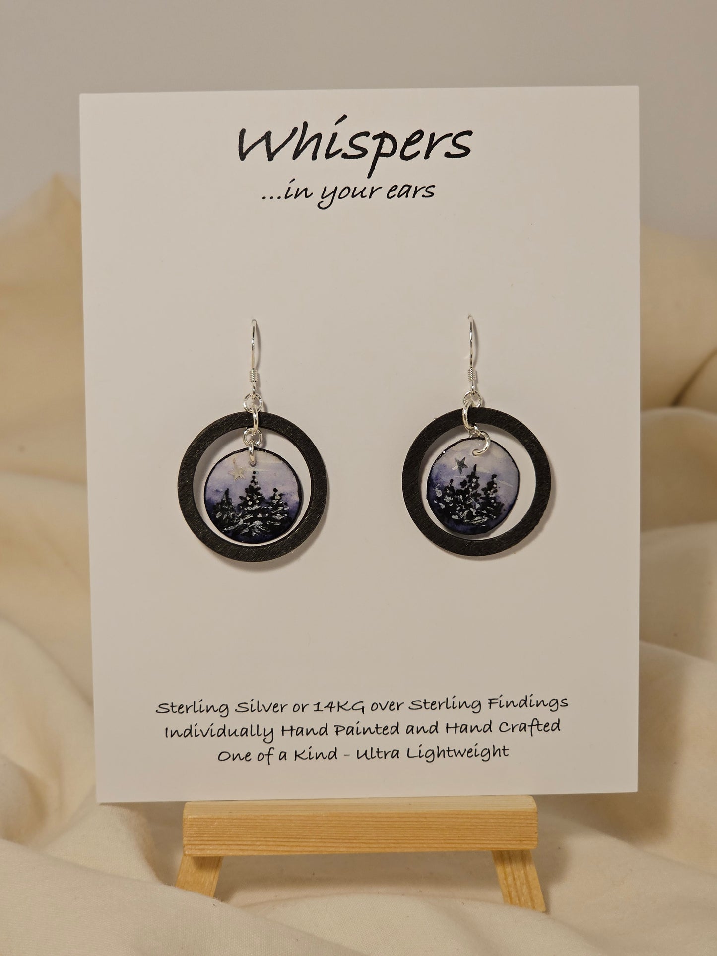 Evening Winter Scape Wood and Paper Earrings. 1 1/8" wood ring painted black. Hanging hand painted watercolor tree silhouette winter scape. Embellished with golden moon. Back is painted with complimentary design. Resin coating for durability. Sterling silver findings. Hangs 1 3/8" in length