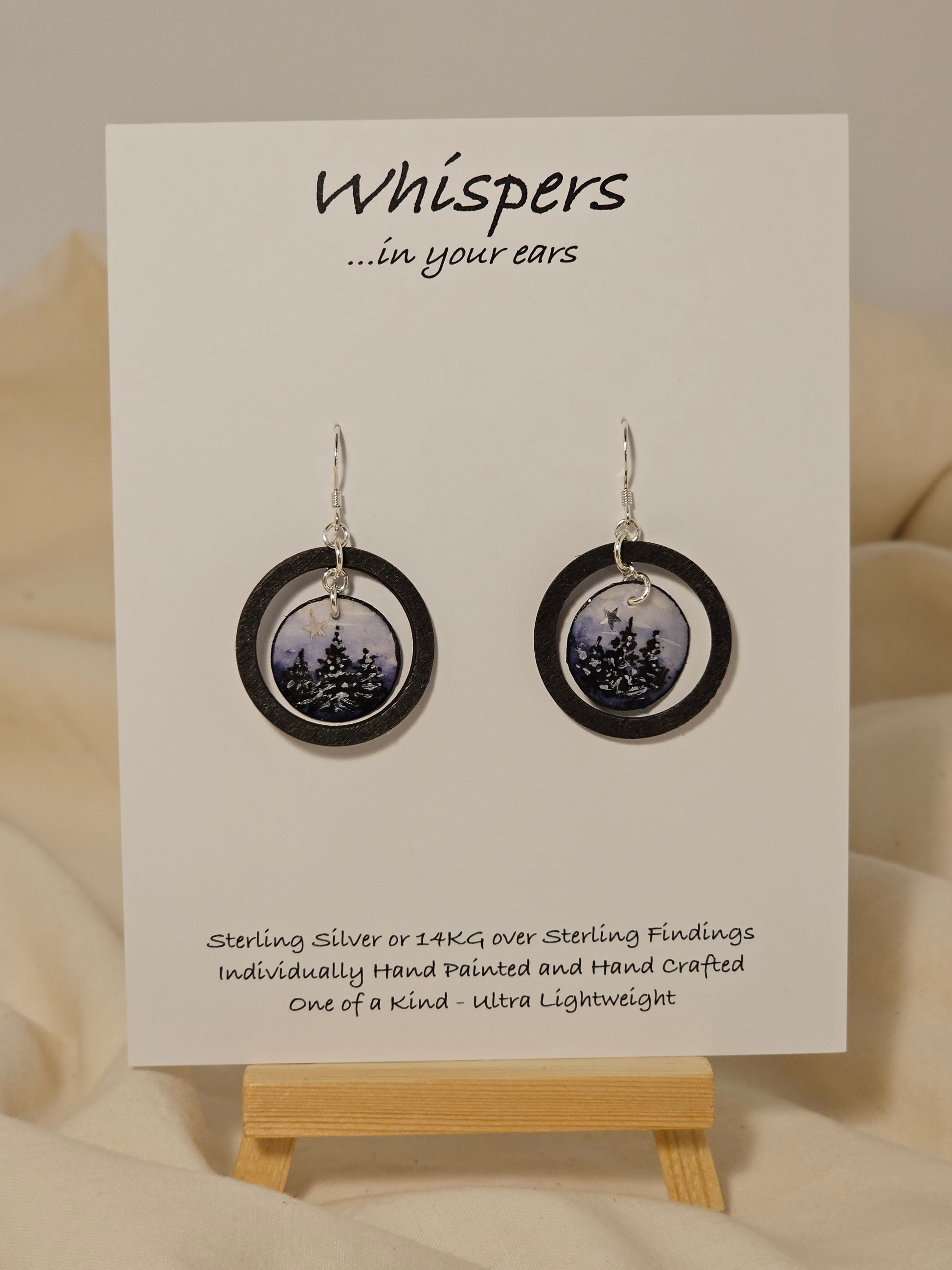 Evening Winter Scape Wood and Paper Earrings. 1 1/8" wood ring painted black. Hanging hand painted watercolor tree silhouette winter scape. Embellished with golden moon. Back is painted with complimentary design. Resin coating for durability. Sterling silver findings. Hangs 1 3/8" in length