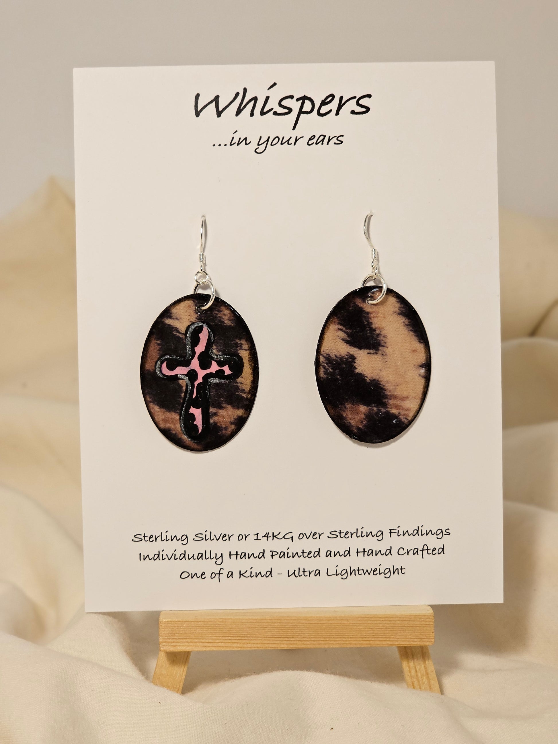 Pink Leopard Cross Hand Painted Paper Earrings. 1 1/2" Oval shaped, Leopard print background with pink leopard print cross. Back is leopard only. Resin coating for durability. Sterling Silver findings. Hangs 1 3/4" in length
