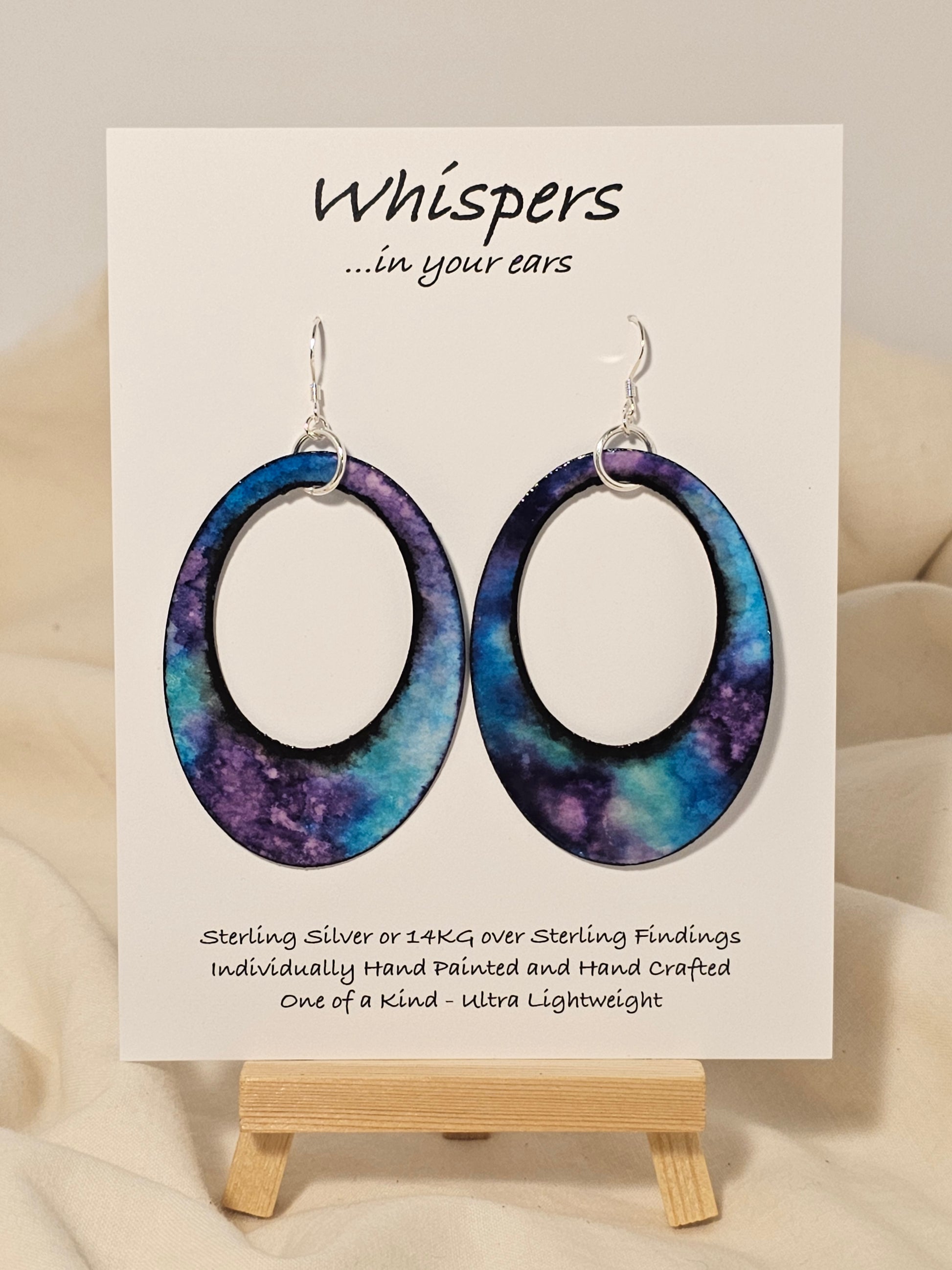 Galaxy Statement Hand Painted Paper Earrings. 2 1/2" Oval with cut out.&nbsp; Statement. Watercolor painted turquoise blue, aqua and purple. Back is painted to match. Edged in black. Resin coating for durability. Sterling Silver findings. Hangs 2 3/4" in length