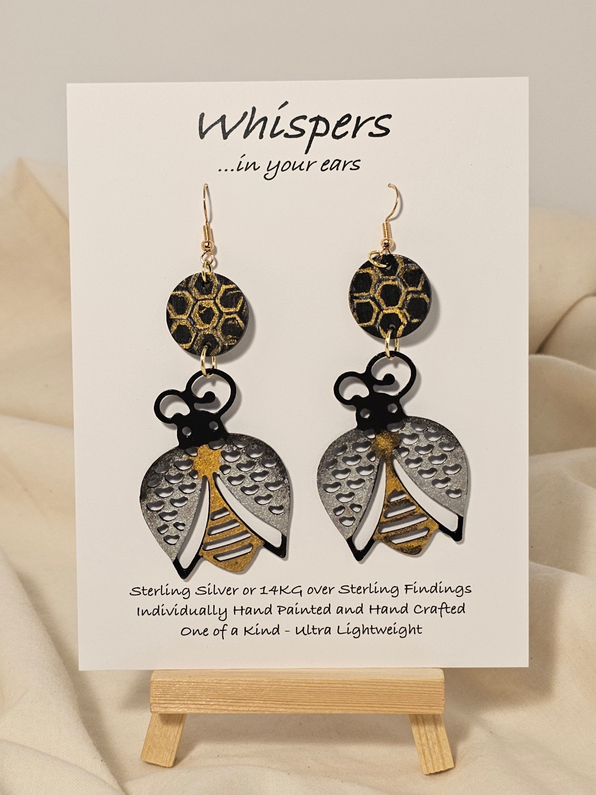 Bee Golden Wood Die Cut Hand Painted Earrings. Honeycomb in gold and black painted wood disc. Metallic painted bee wood die cut. Back is painted to match. Enameled for durability. 14KG over sterling silver findings. Hangs 3" in length