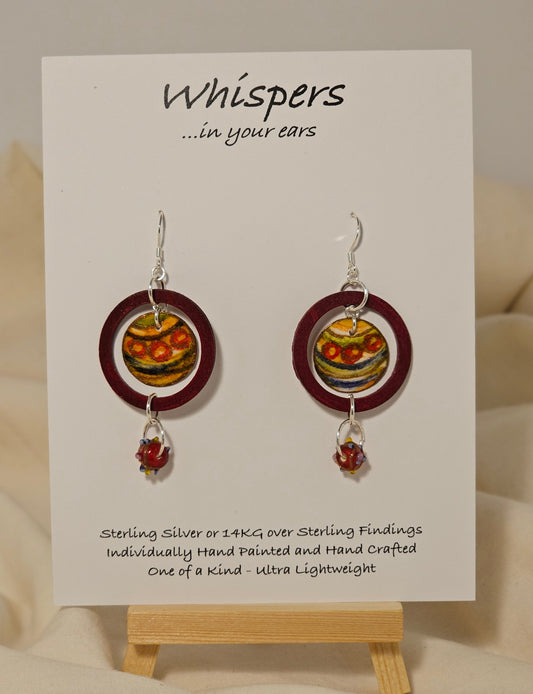 Red Ornament Ring Wood and Paper Earrings. 1 1/4" painted red wood ring with hanging hand painted watercolor ornament in the center. Multicolored glass bead hanging at the bottom. Back is painted in complimentary design. Enameled for durability. Sterling Silver findings. Hangs 2" in length