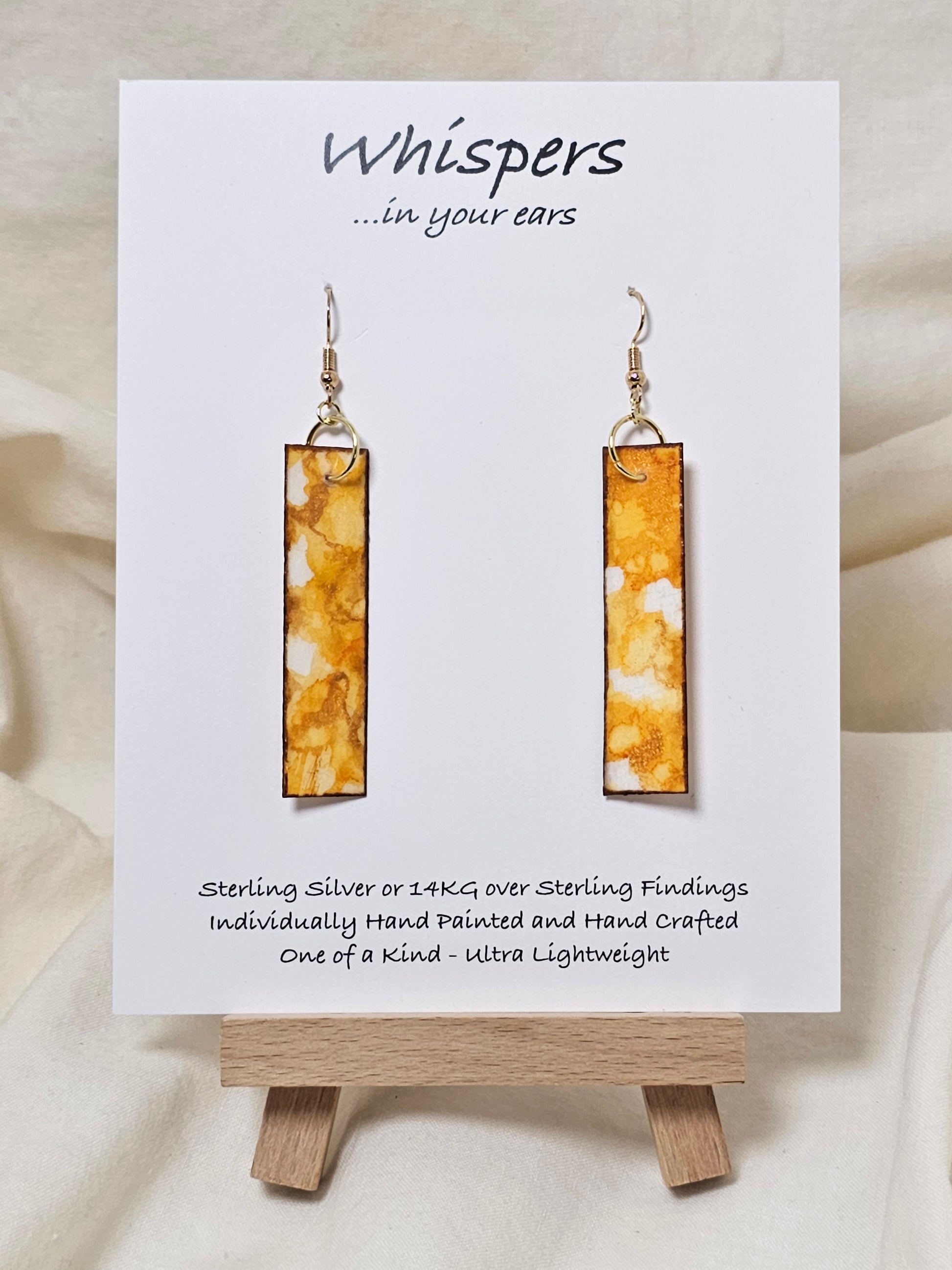 Yellow Citrine Geode Hand Painted Paper Earrings. 1/2" x 2" Elongated Rectangle painted in yellows and metallic gold, faux citrine geode. Edged in gold. Back is painted in similar design. Resin coating for durability. Mixed metal findings, 14KG over sterling wires. Hangs 2 1/4" in length