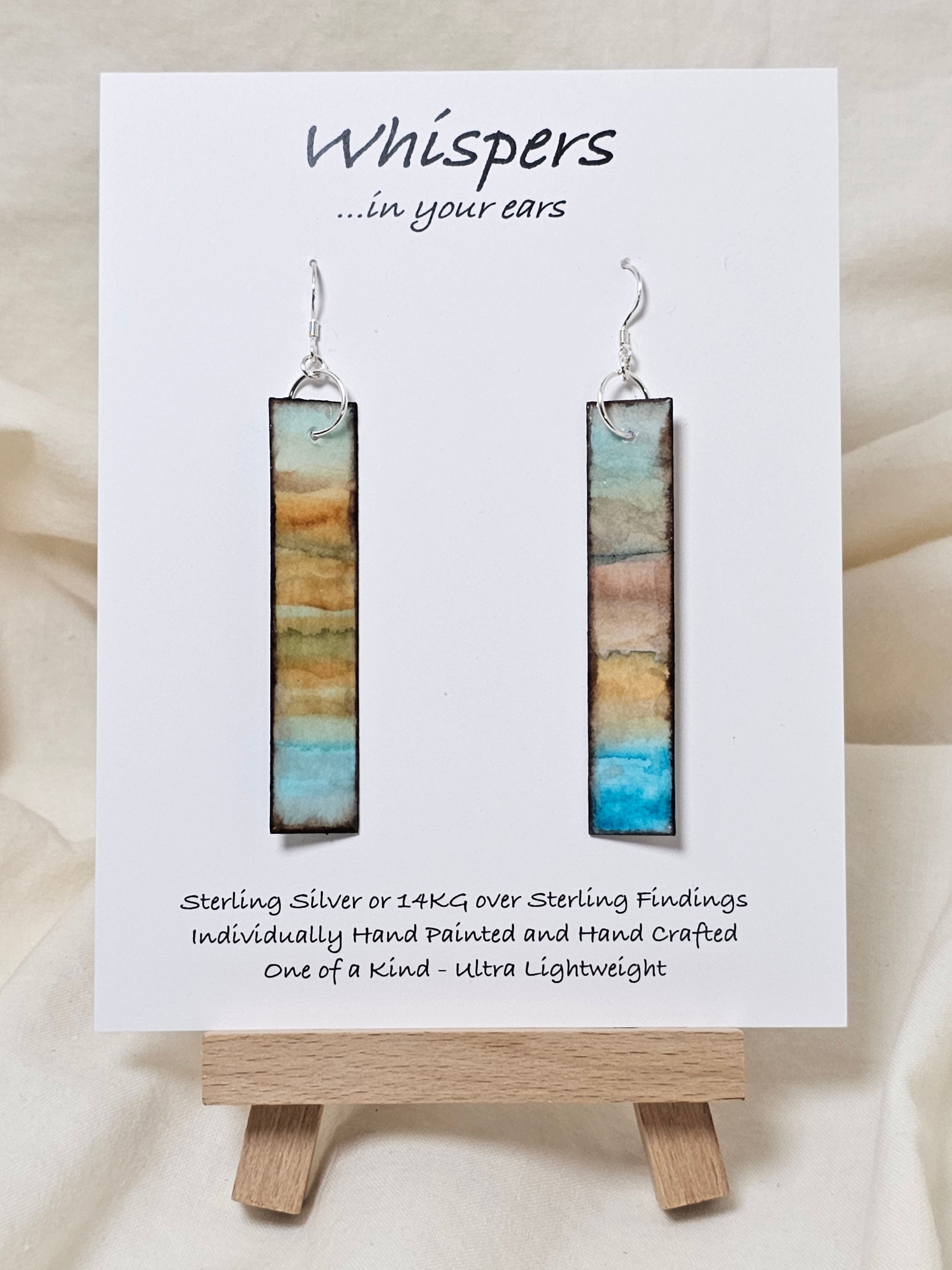 Vintage Beach Reflections Hand Painted Paper Earrings. Ultra lightweight 1/2" x 2 1/2" elongated rectangle. Watercolor abstract beach reflection. Distressed edge in brown. Back is painted with similar design. Resin coating for durability. Sterling Silver findings. Hangs 2 3/4" in length