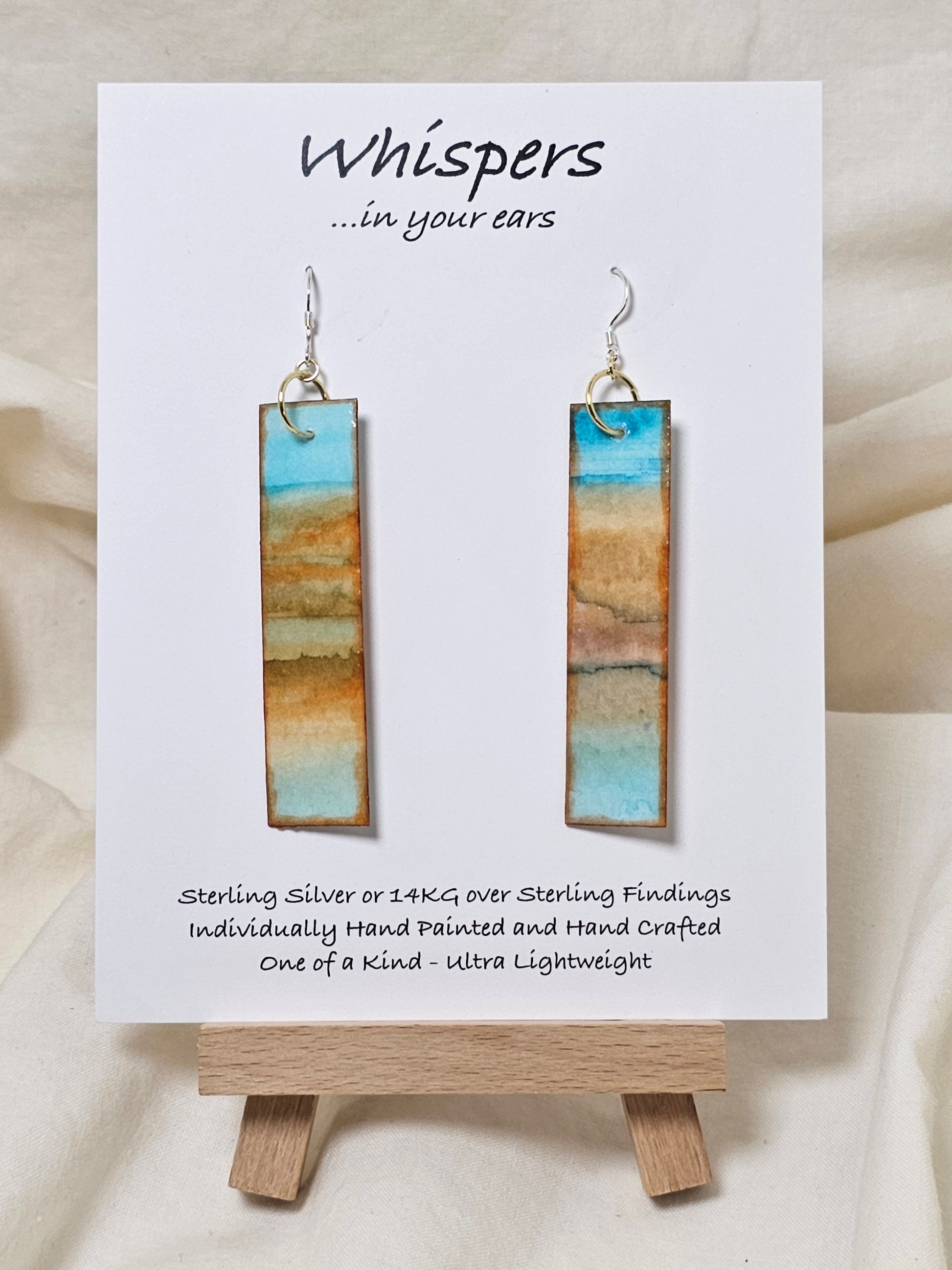 Beachscape Reflection Statement Hand Painted Paper Earrings. Abstract beachscape painted in and on heavy watercolor paper. 1/2" x 2 1/2" elongated rectangle. In muted blues and beiges and corals. Reflection of landscape. Resin coating for durability. Sterling silver ear wires and findings. Ultra lightweight. Hangs 2 3/4"