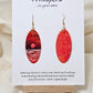 Red Sky Morning Hand Painted Paper Earrings. Ultra lightweight elongated 2" oval. Watercolor red, orange, white and gold sunrise over water. Back painted in similar color. Resin coating for durability. 14KG over sterling findings. Hangs 2 1/4" in length