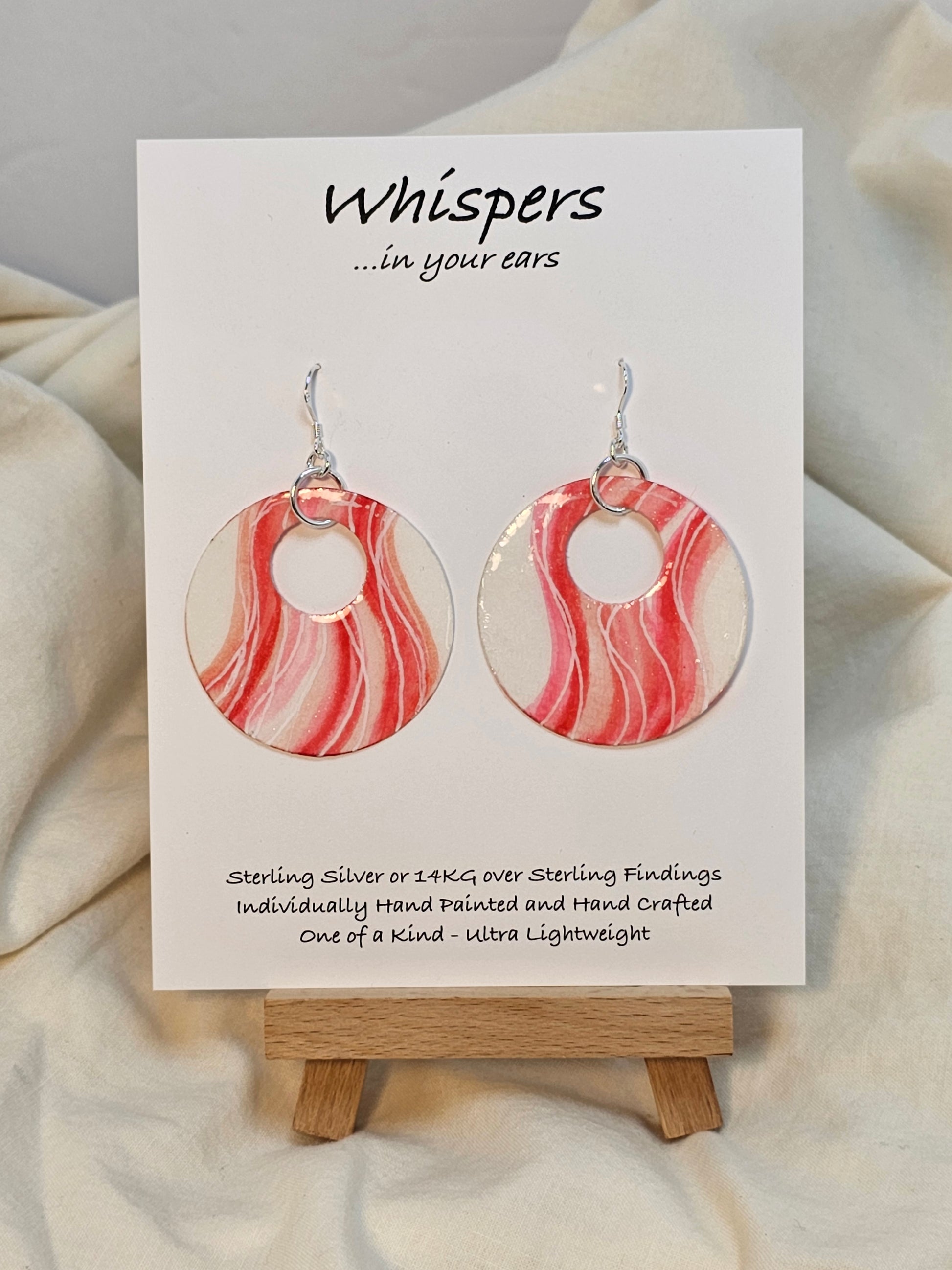 Sweet Swirls Hand painted watercolor paper earrings. Ultra lightweight. Dark pink, light pink, peach and white wavy stripes over a white background. Back is painted with similar color and design. Large circular in shape with circular cut out. Resin coating for durability. Sterling silver findings. Hangs 2" in Length