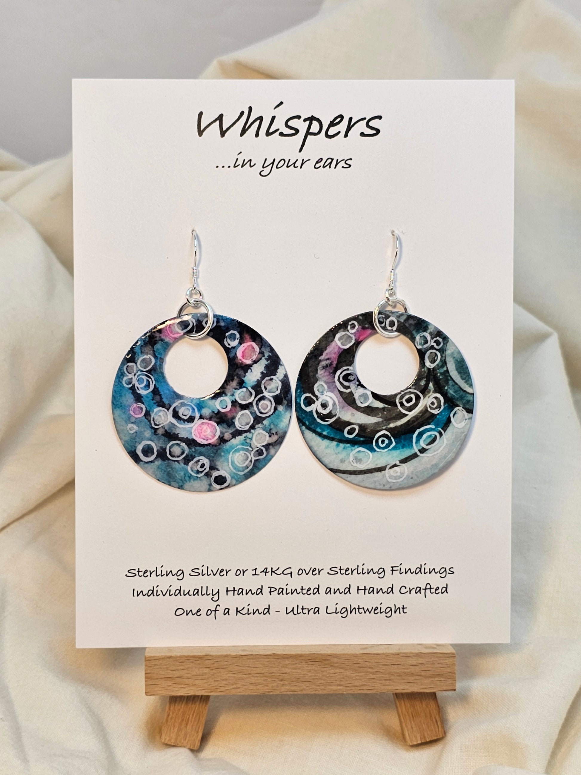 Bubbles Hand painted watercolor paper earrings. Ultra lightweight. Dark blue, pink, light pink, turquoise with white circles . Back is painted with similar color and design. Large circular in shape with circular cut out. Resin coating for durability. Sterling silver findings. Hangs 2" in Length