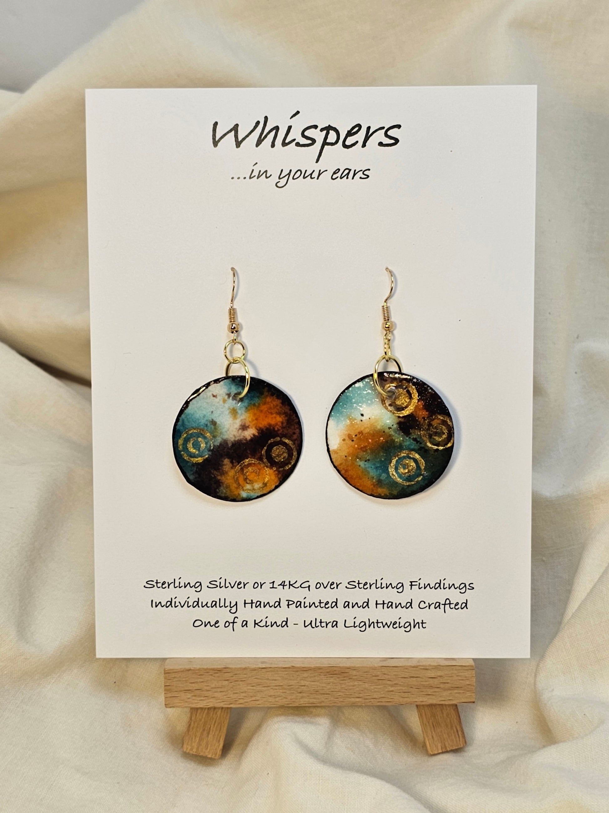 Gold Bullseye Hand Painted Watercolor Paper Earrings. Ultra lightweight 1 1/4" Circle abstract watercolor painting Deep blue, orange, brown and metallic gold bullseye accents. Back is painted to match. Edged in dark brown. Resin coating for durability. 14KG over sterling findings. Hangs 1 5/8" in length