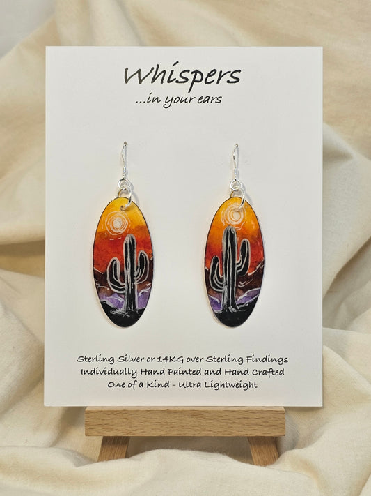 Desert Sunset Hand Painted Paper Earrings.&nbsp; Ultra lightweight 2" Elongated oval. Features Cactus in silhouette. Vibrant orange yellow and purple sky. Painted dark edge. Back is painted with similar color. Resin coating for durability. Sterling Silver findings. Hangs 2 1/8" in length