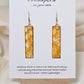 Yellow Citrine Geode Hand Painted Paper Earrings. 1/2" x 2" Elongated Rectangle painted in yellows and metallic gold, faux citrine geode. Edged in gold. Back is painted in similar design. Resin coating for durability. Mixed metal findings, 14KG over sterling wires. Hangs 2 1/4" in length