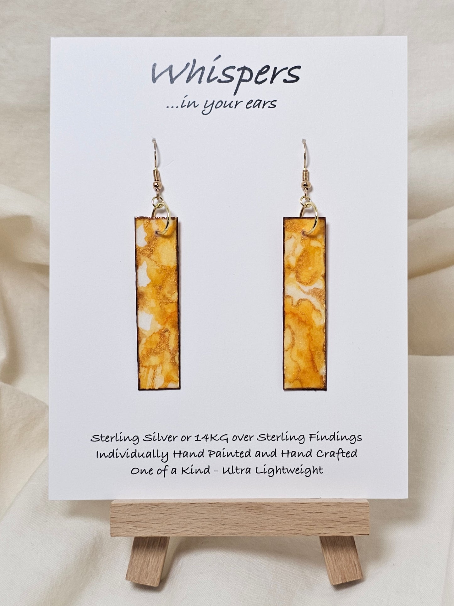 Yellow Citrine Geode Hand Painted Paper Earrings. 1/2" x 2" Elongated Rectangle painted in yellows and metallic gold, faux citrine geode. Edged in gold. Back is painted in similar design. Resin coating for durability. Mixed metal findings, 14KG over sterling wires. Hangs 2 1/4" in length