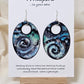 Cosmic Energy Hand Painted Paper Earrings.&nbsp; Ultra lightweight 2 1/2" Statement Oval with small circular cut out. Watercolor blues, greens and black. Abstract design. Back is painted in similar colors. Resin coating for durability. Sterling Silver findings. Hangs 2 3/4" in length