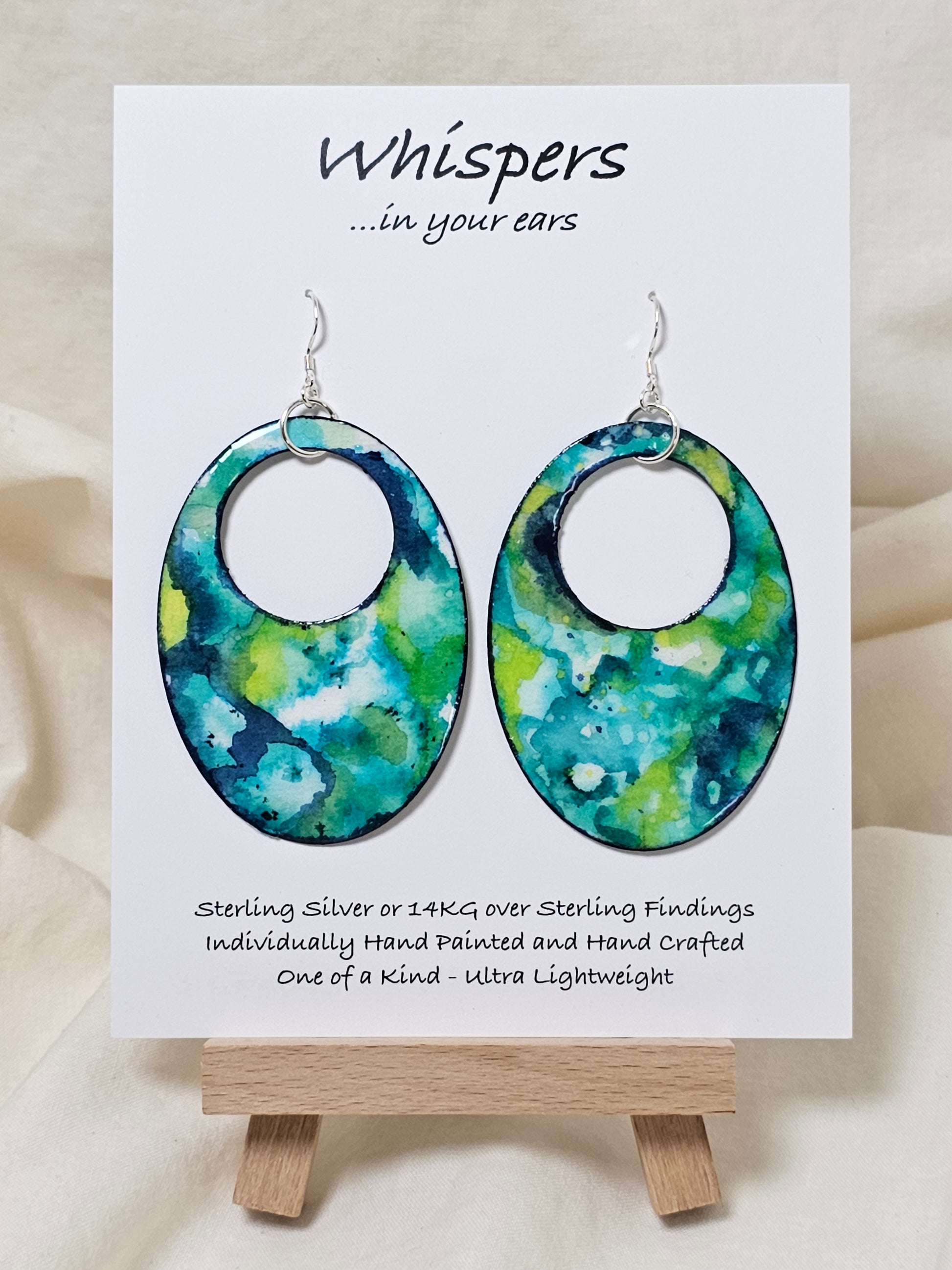 Caribbean Waters Hand Painted Paper Earrings. Ultra lightweight 2 1/2" Statement Oval with medium circular cut out. Watercolor blues, greens and turquoise. Abstract design. Back is painted in similar colors. Resin coating for durability. Sterling Silver findings. Hangs 2 3/4" in length
